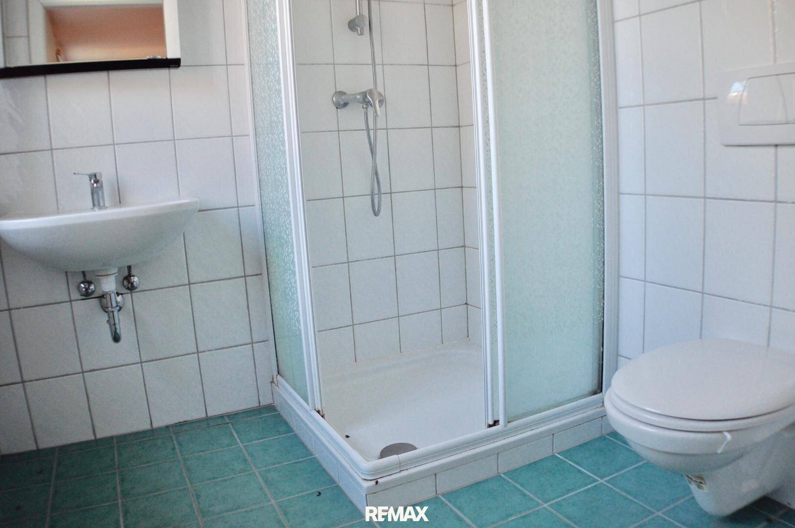 Badezimmer mit Duschkabine, Waschbecken und WC, komplett gefliest in Weiß und Grün, funktional.