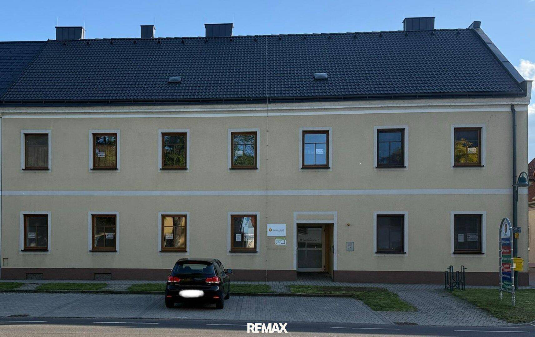 Vorderansicht des Gebäudes mit mehreren Fenstern und einem geparkten Auto davor auf dem Parkplatz.
