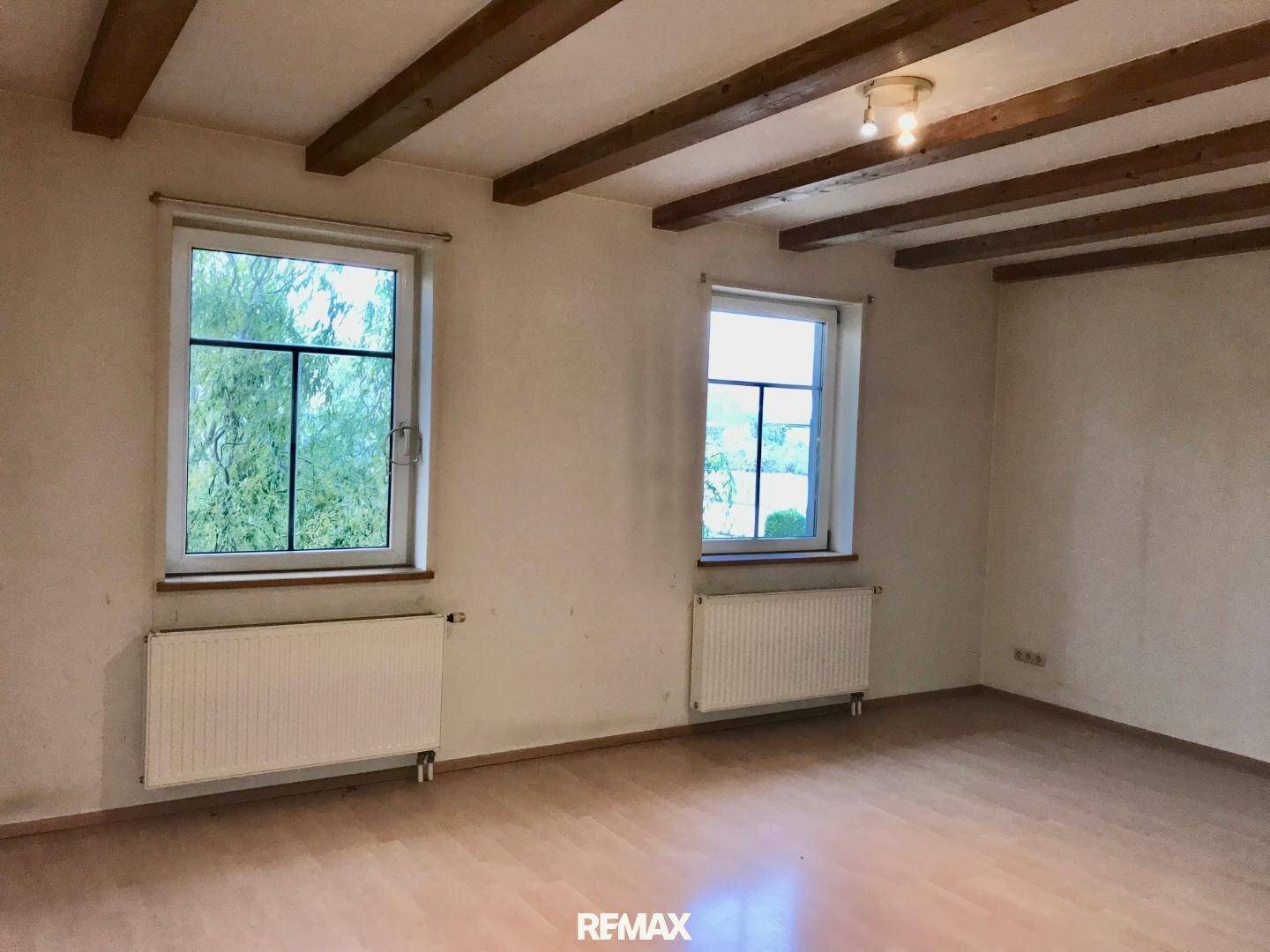 Geräumiger Wohnraum mit sichtbaren Holzbalken an der Decke und Laminatboden, rustikaler Charme.