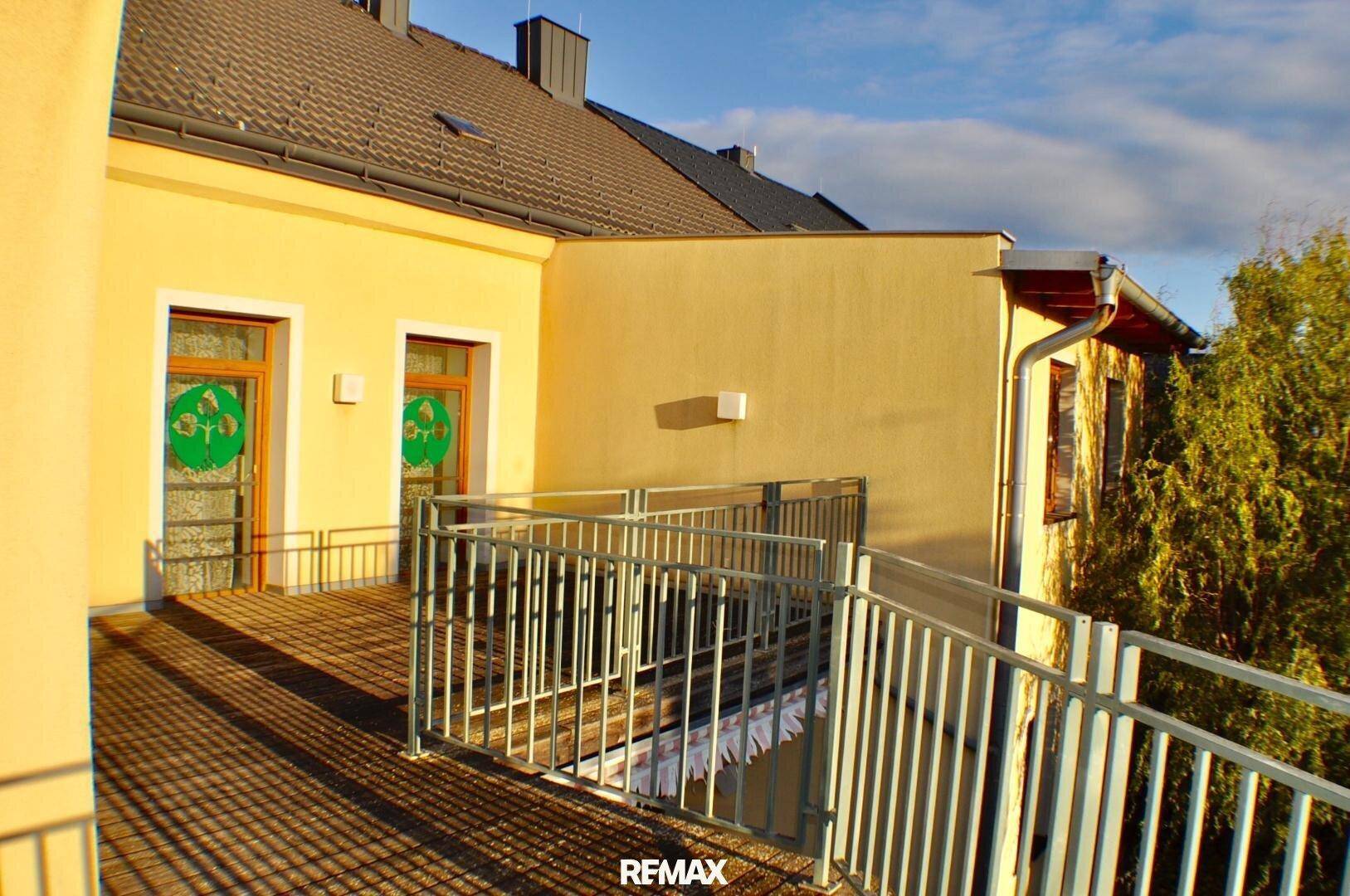 Großer Balkon mit Metallgeländer und Zugang zu den Innenräumen des Gebäudes, sonnig und geräumig.