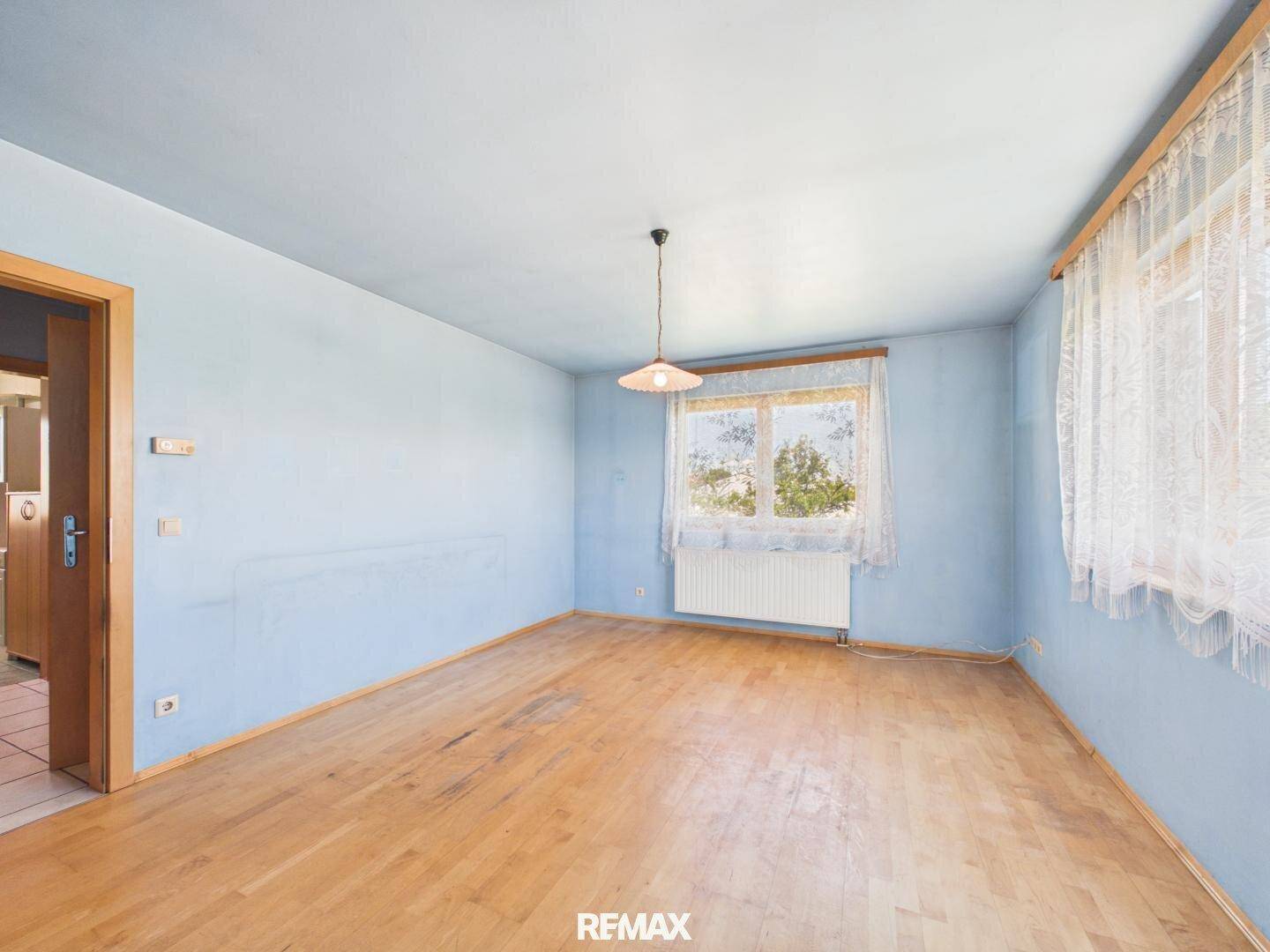Geräumiges Wohnzimmer mit Holzboden, hellblauen Wänden und großem Fenster für viel Tageslicht.