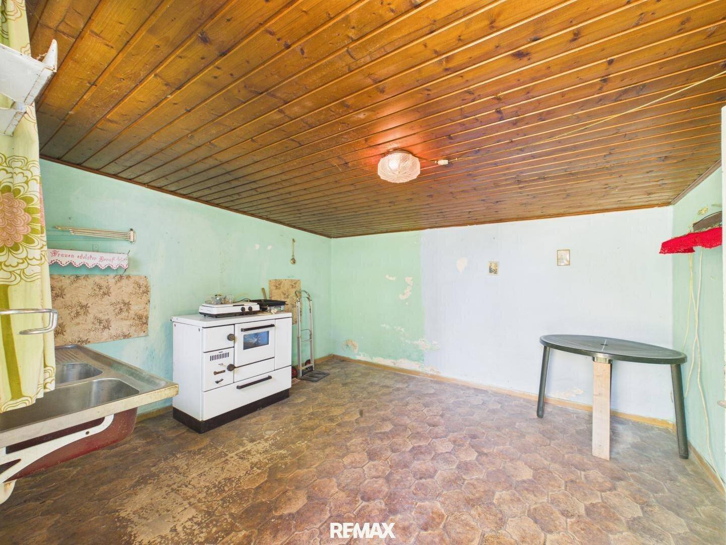Funktionaler Raum mit Holzdecke, Spüle und traditionellem Ofen, ideal als Hauswirtschaftsraum.