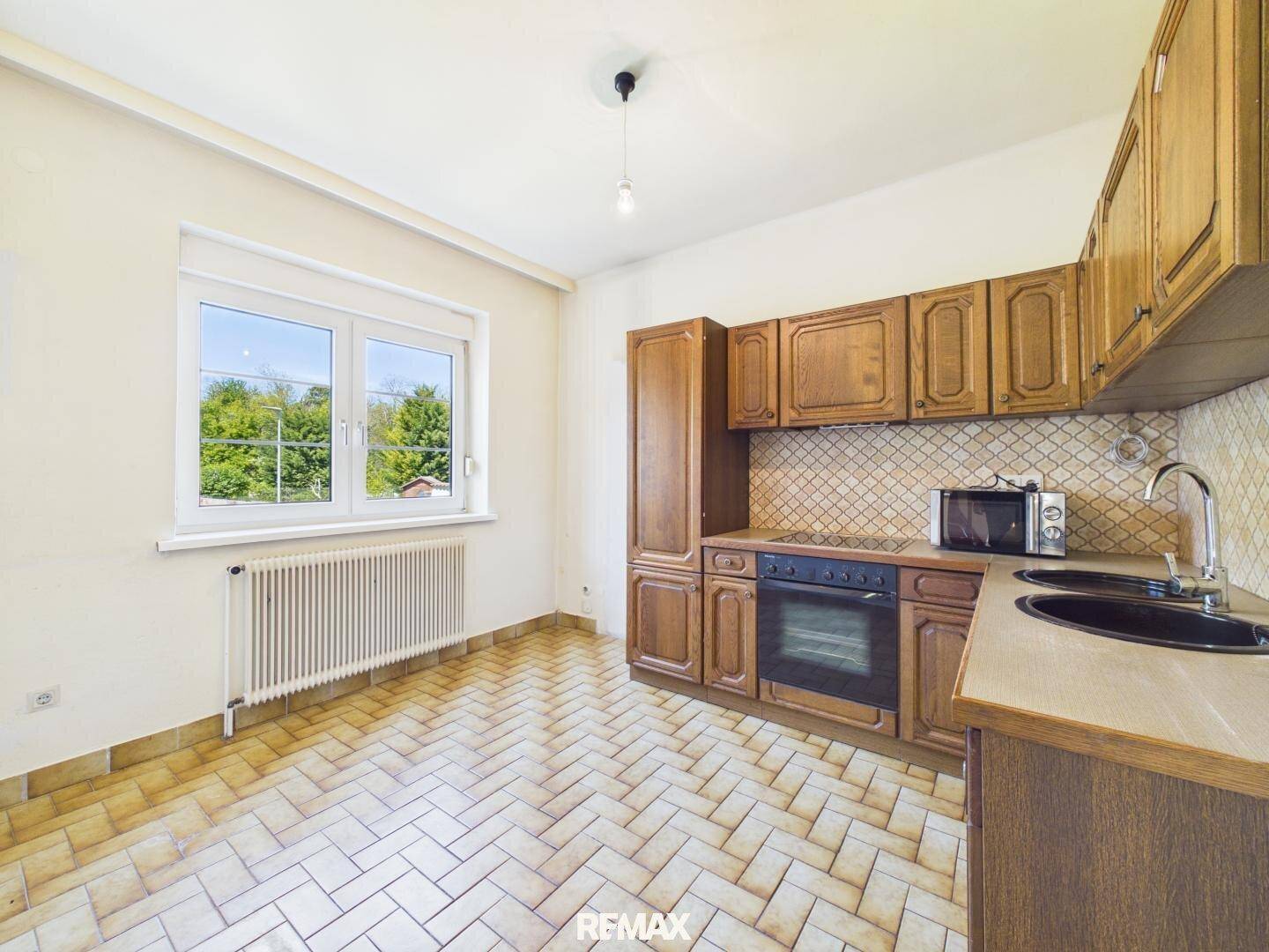 Küche mit Holzschränken, Terrakottafliesen und einem Fenster mit Blick ins Grüne.