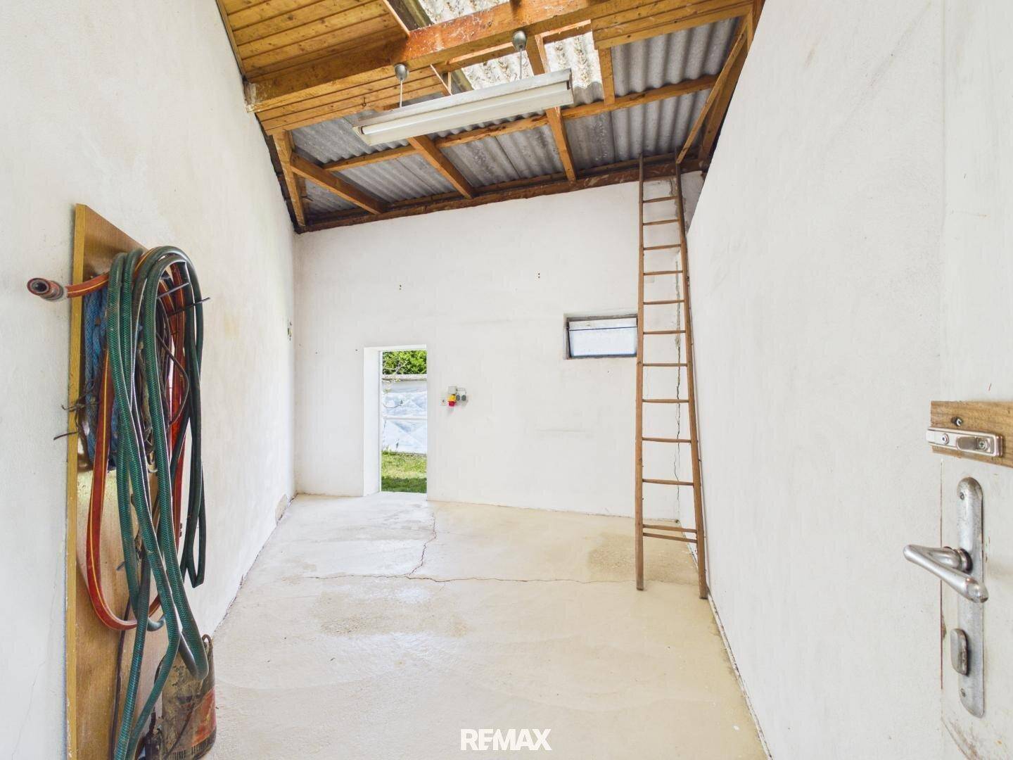 Geräumiger Werkstattraum mit hoher Decke, Leiter und Blick ins Grüne durch die offene Tür.