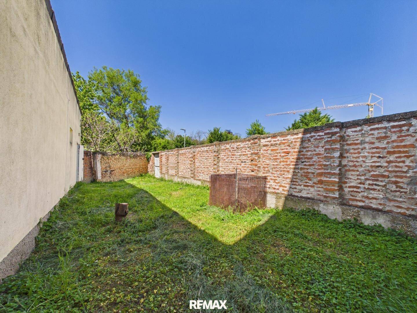 Hinterhof mit Rasenfläche und einer alten Ziegelmauer, die das Grundstück begrenzt.