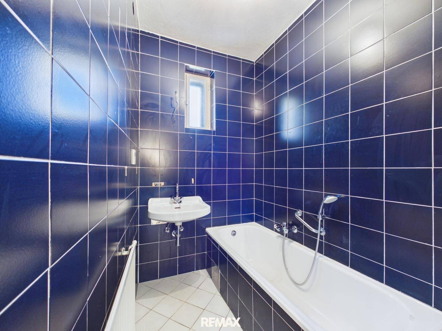 Badezimmer mit dunkelblauen Fliesen, einer Badewanne und einem kleinen Fenster für Tageslicht.