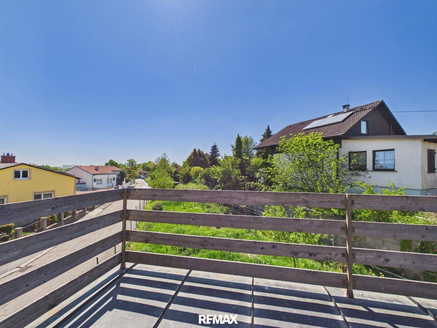 Balkon mit Holzgeländer und weitem Blick über die umliegende Landschaft und Häuser.