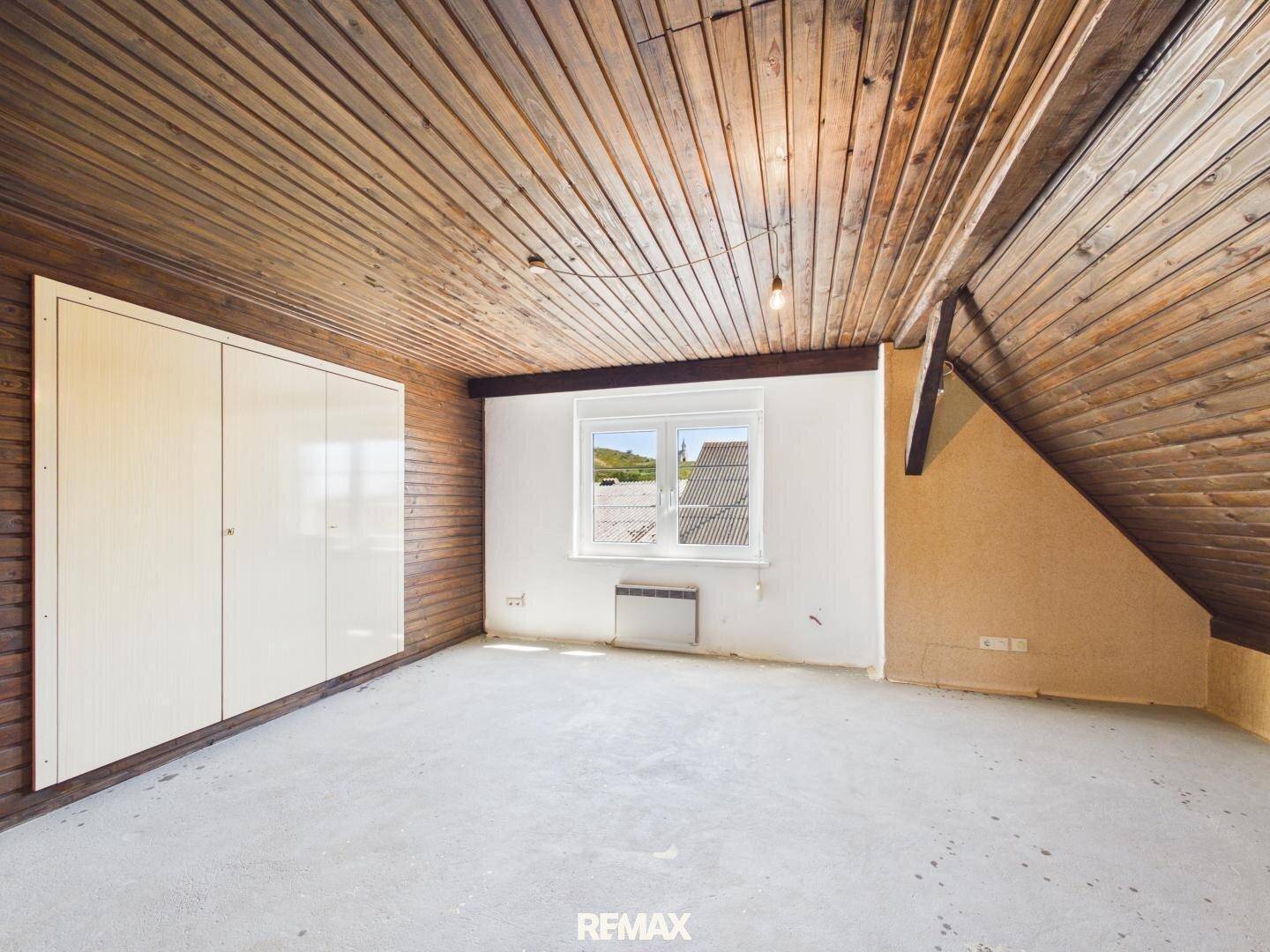 Geräumiges Dachzimmer mit Holzverkleidung, Einbauschrank und einem Fenster mit Ausblick.
