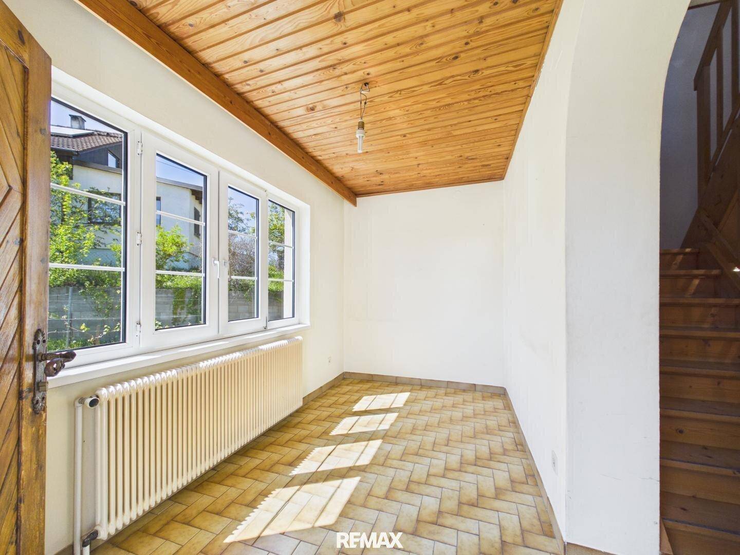Geräumiger Flur mit Holzdecke, Terrakottafliesen und einem Heizkörper unter den großen Fenstern.