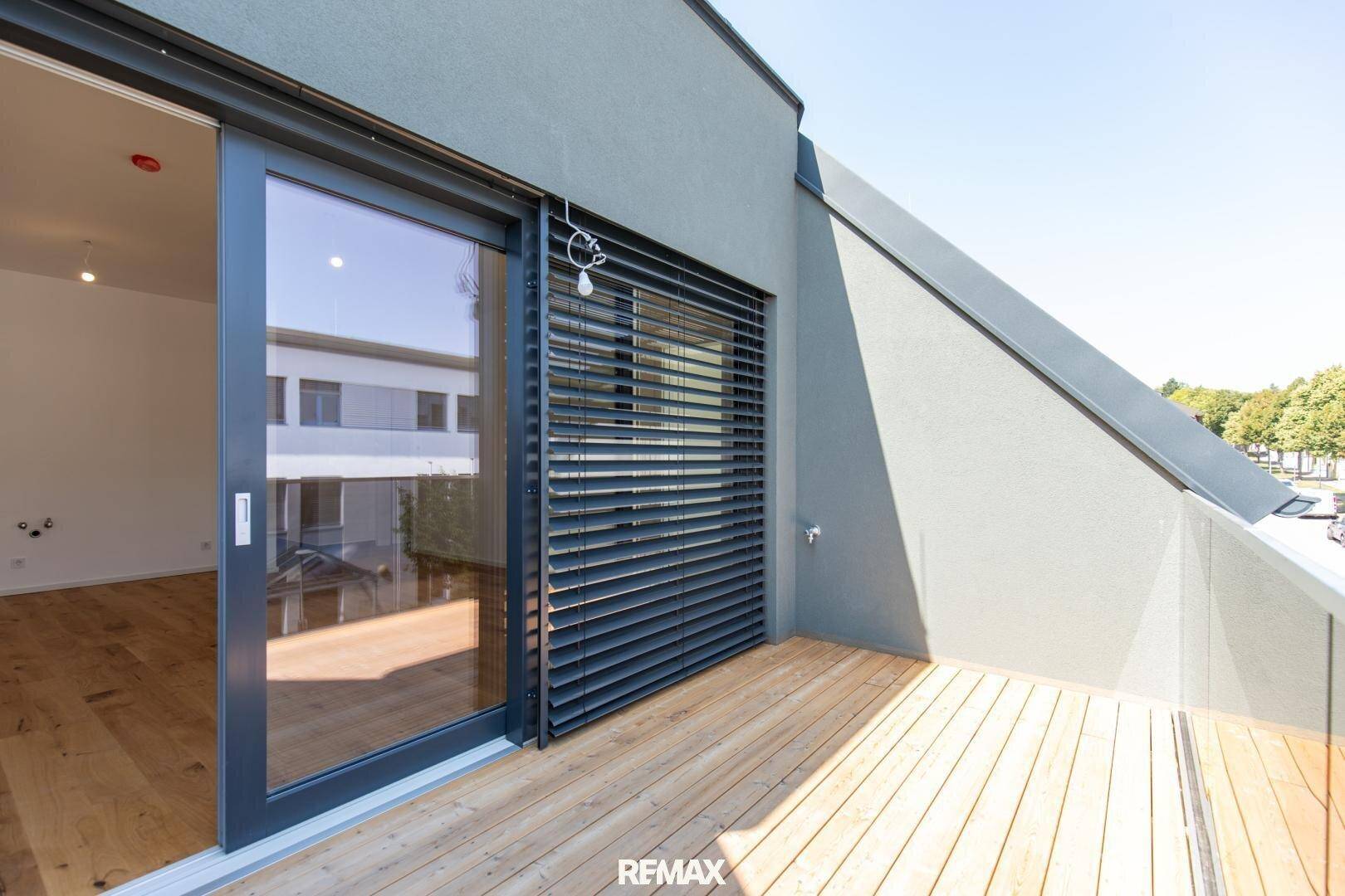 Heller Balkon mit Holzdeck und Schiebetür, ausgestattet mit Außenjalousien.