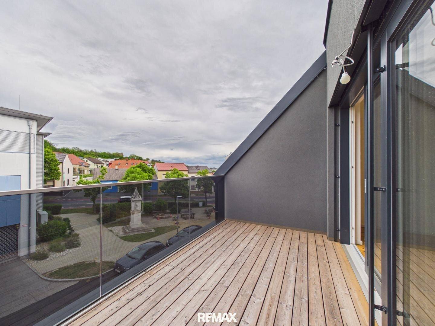 Moderner Balkon mit Holzdeck und Glasgeländer, bietet Blick auf die Umgebung.