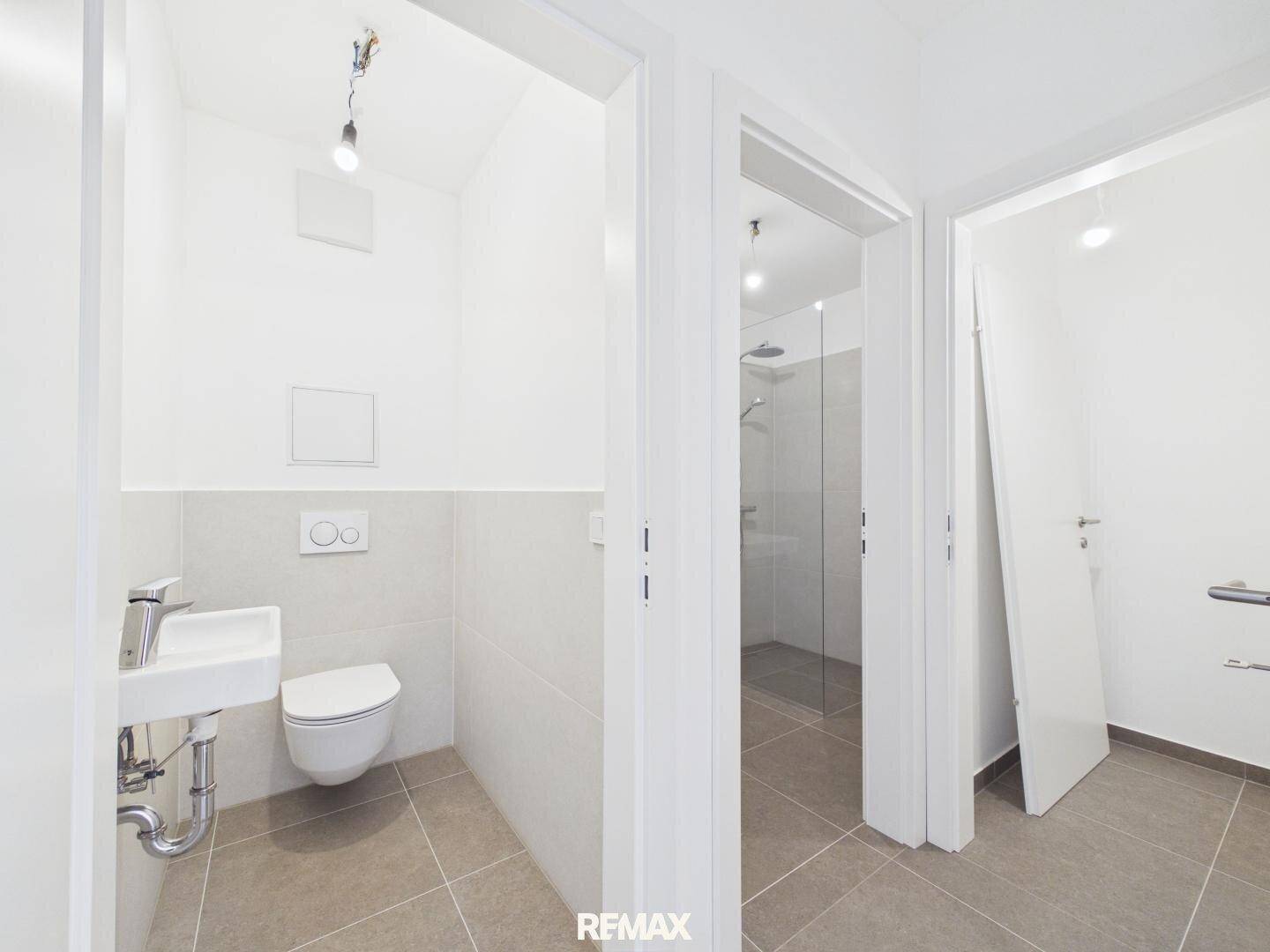 Blick in ein modernes WC und einen separaten Duschbereich mit Fliesenboden.