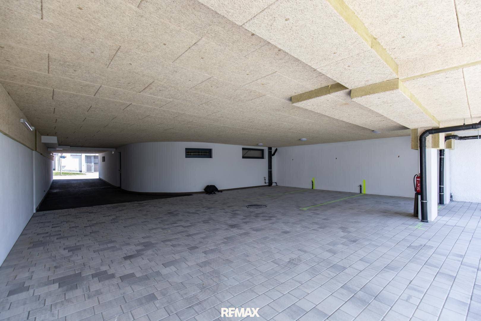 Geräumiger überdachter Parkbereich mit Fliesenboden unter dem Gebäude.
