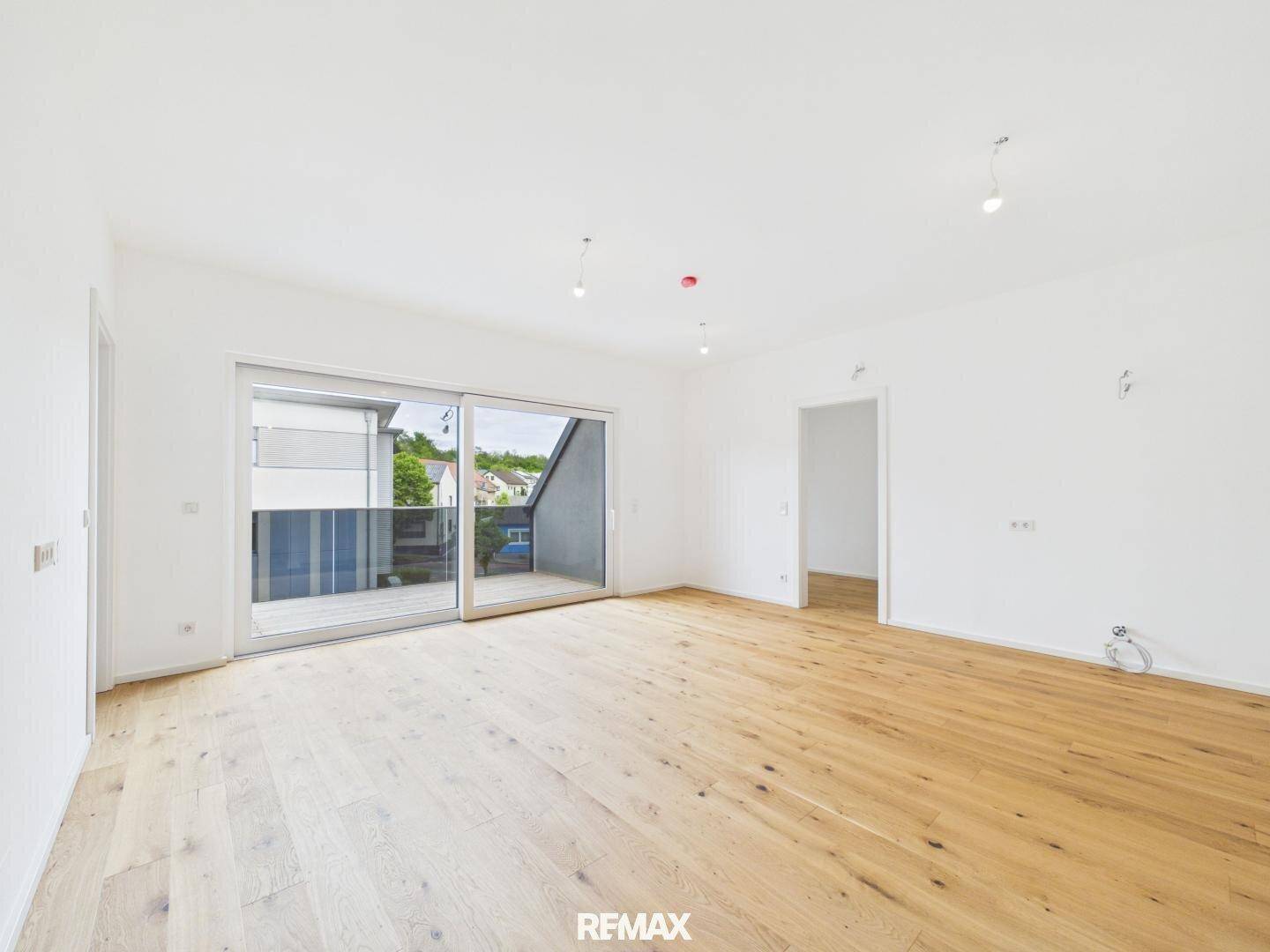 Geräumiger, heller Wohnbereich mit Holzboden und Zugang zu einem Balkon.