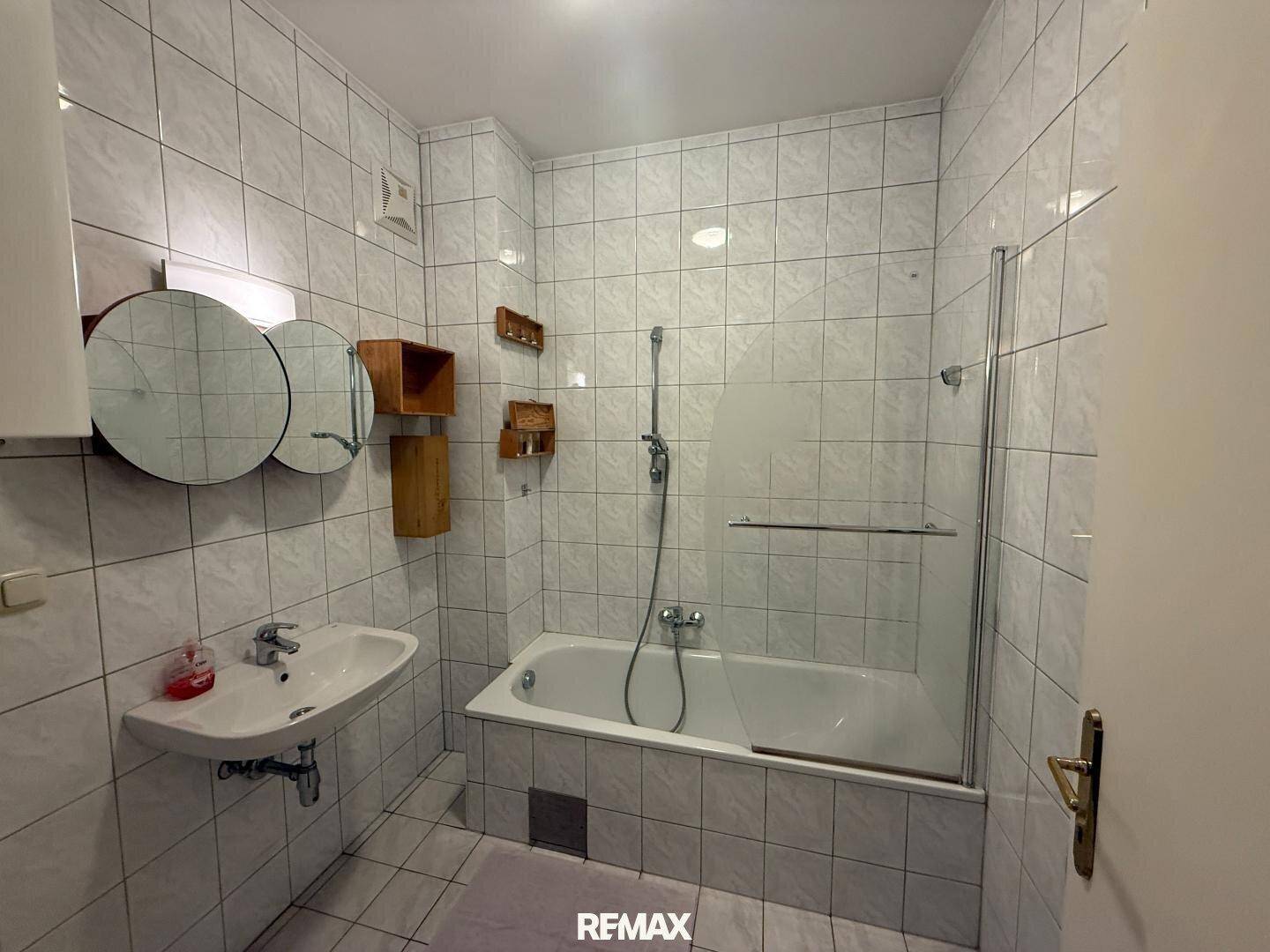 Gefliestes Badezimmer mit Badewanne, Duschabtrennung und Waschbecken.