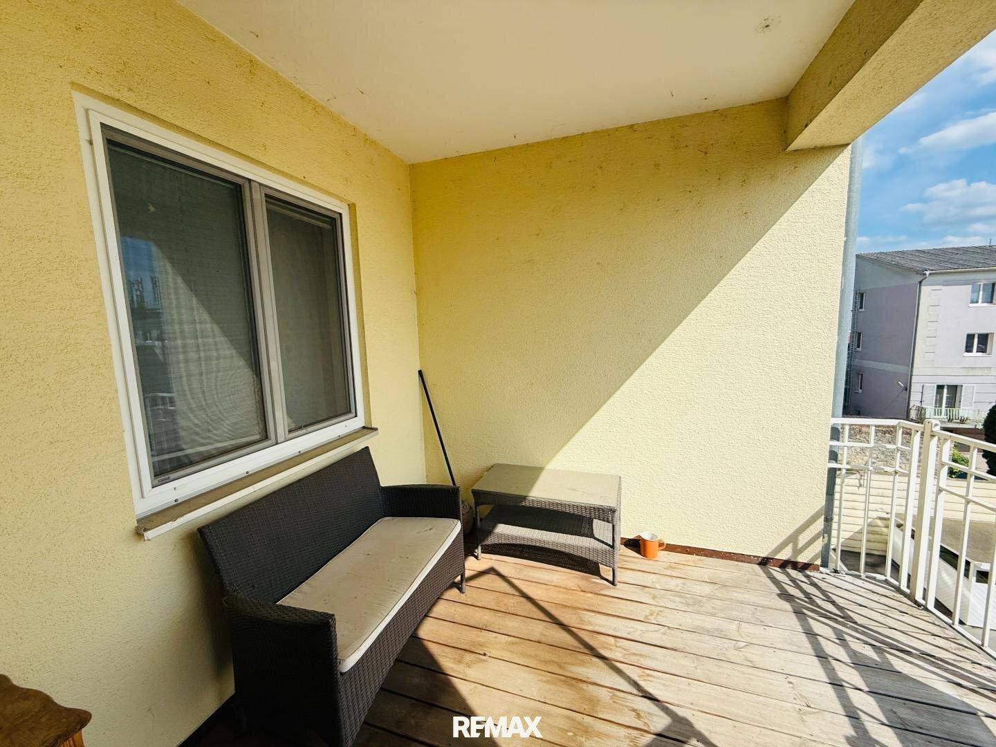 Sonniger Balkon mit Sitzgelegenheit und Holzboden, ideal zum Entspannen im Freien.