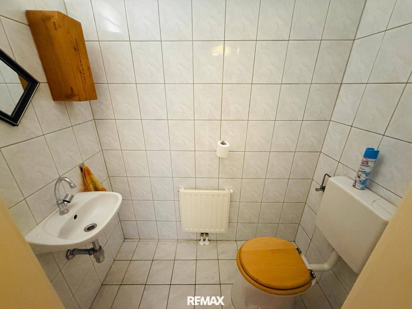Separates WC mit Waschbecken, Heizkörper und gefliesten Wänden und Boden.