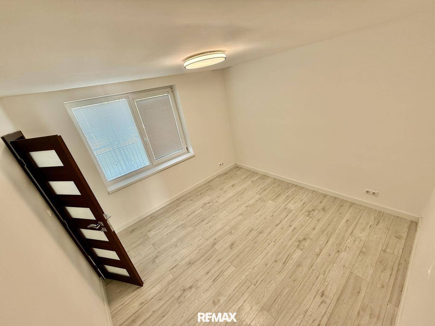 Helles Schlafzimmer mit Laminatboden und Fenster mit Jalousien, bereit zur Einrichtung.