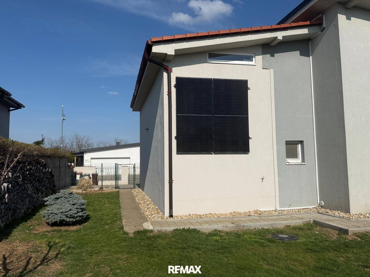 Seitenansicht des Hauses mit Photovoltaik-System an der Fassade und grünem Rasen.