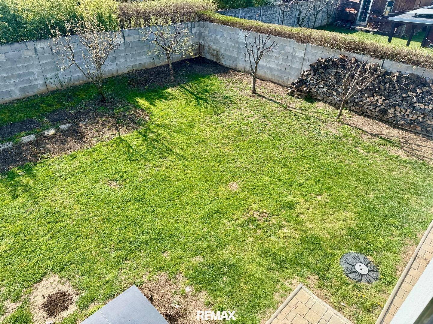 Grüner Gartenbereich mit Rasenfläche, jungen Bäumen und einer Holzstapelwand.
