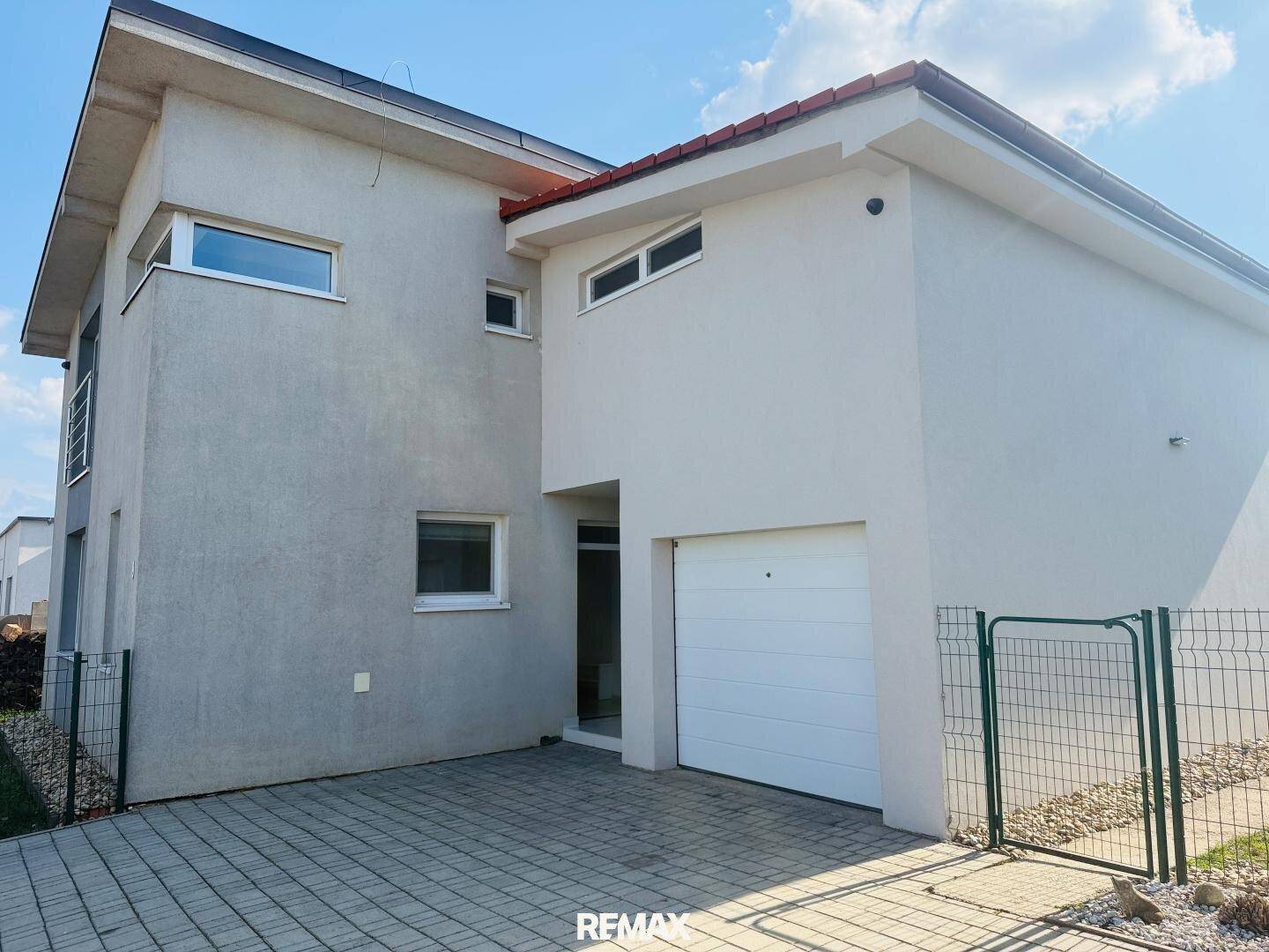 Modernes Haus mit Garagentor und gepflasterter Einfahrt, umgeben von einem Zaun.
