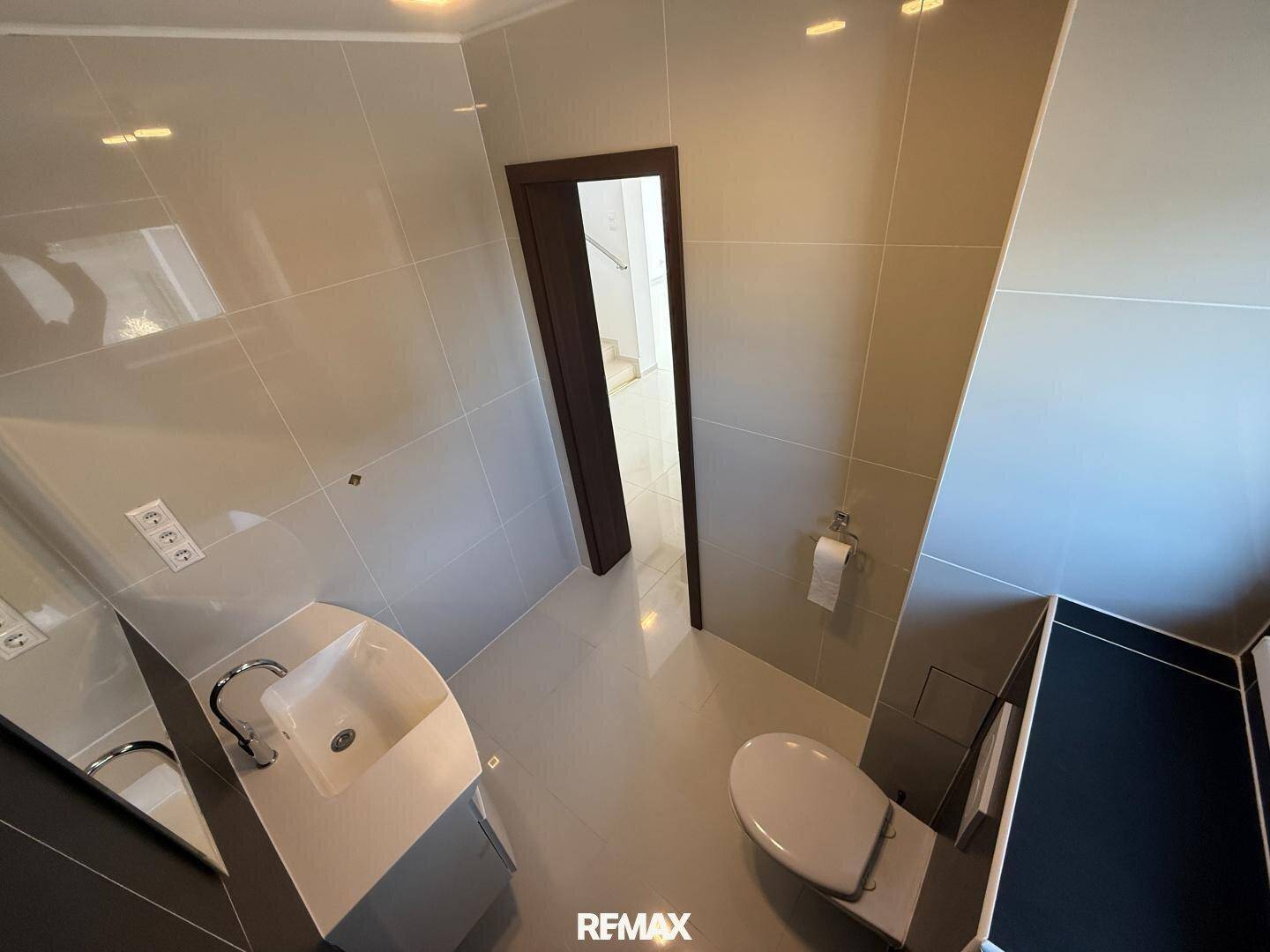 Modernes Gäste-WC mit Wand-WC, kleinem Waschbecken und hellen Fliesen.