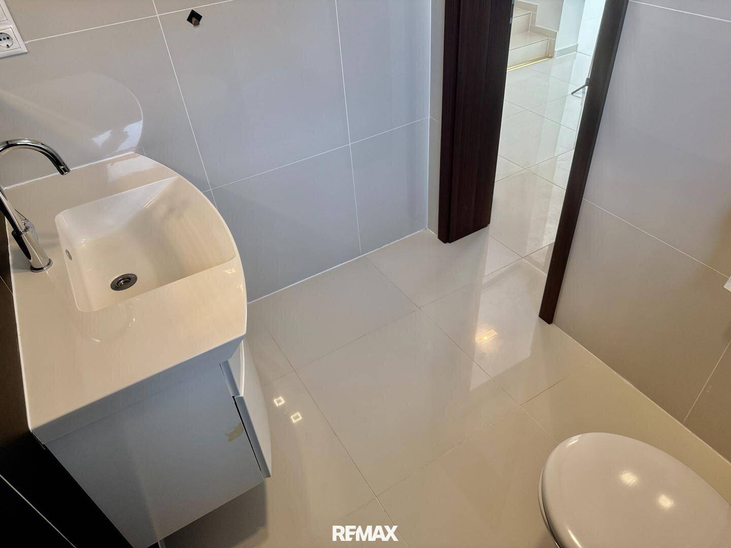 Helles Gäste-WC mit modernem Waschbecken, Wand-WC und glänzenden Fliesen.