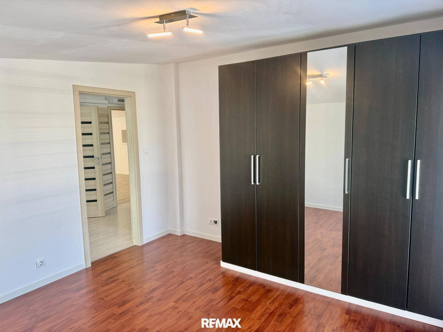 Schlafzimmer mit dunklem Laminatboden, Spiegelschrank und Zugang zu weiteren Räumen.