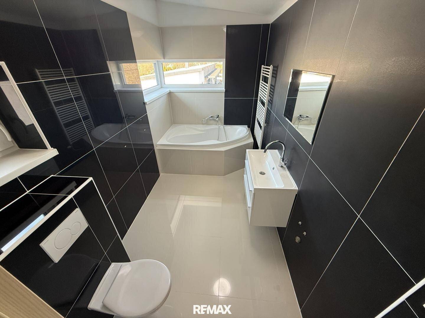 Modernes Badezimmer mit schwarzen Fliesen, Eckbadewanne, Toilette und Waschbecken.