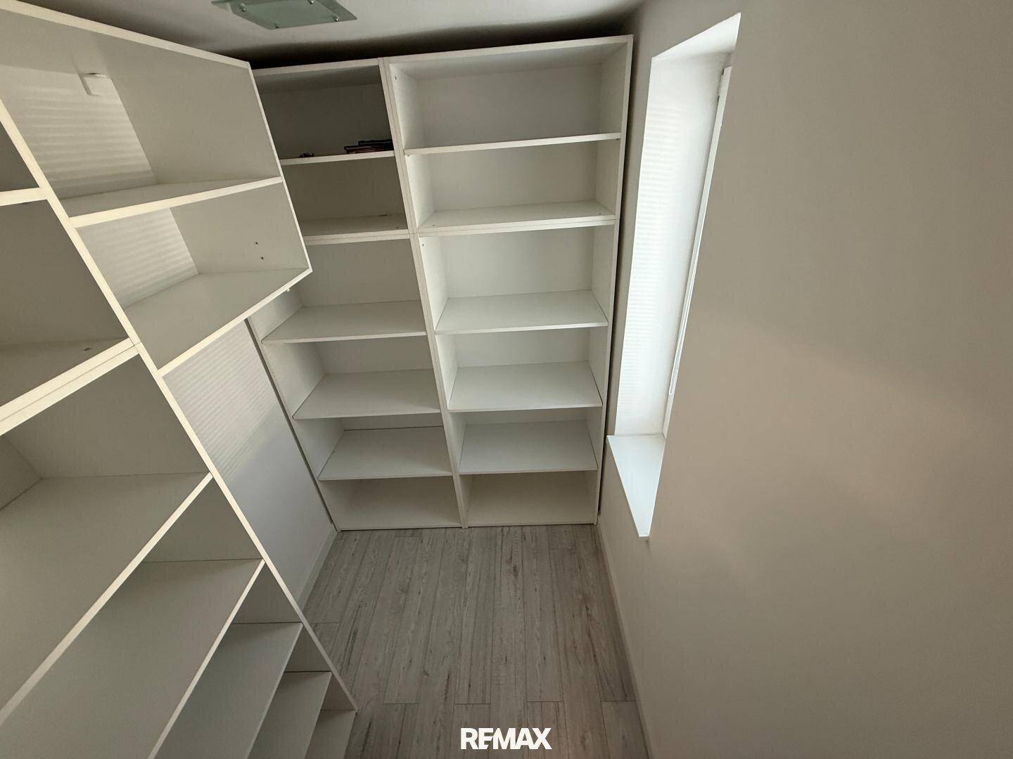 Praktischer begehbarer Kleiderschrank mit vielen offenen Regalen und Laminatboden.