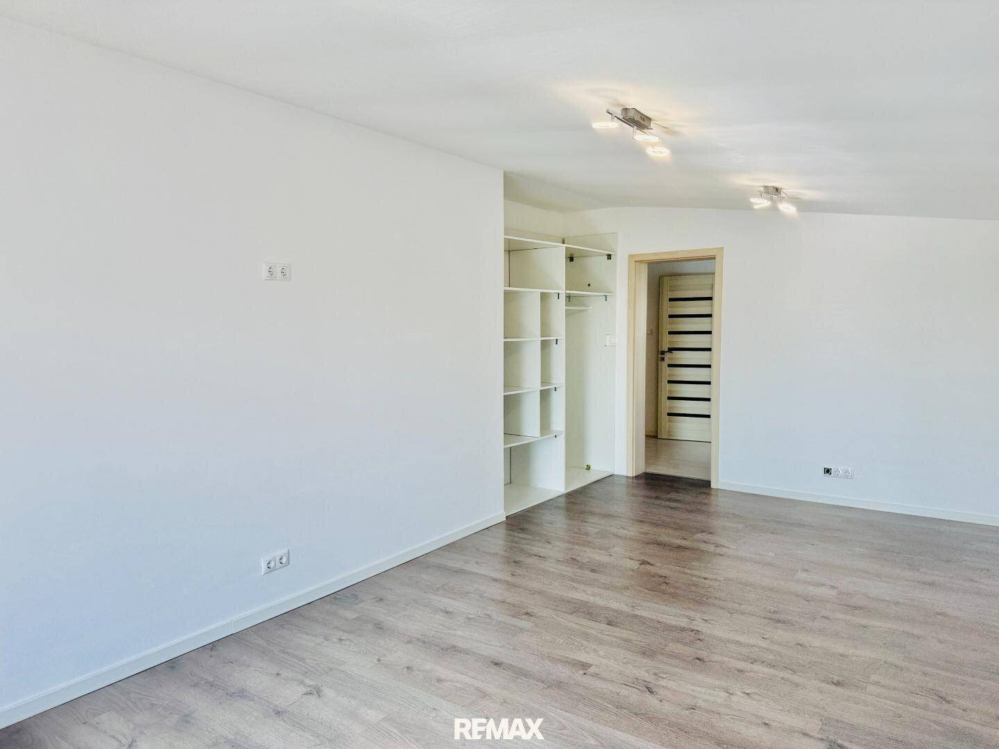 Heller, leerer Raum mit Laminatboden und eingebauten Regalen, ideal als Wohnzimmer oder Flur.