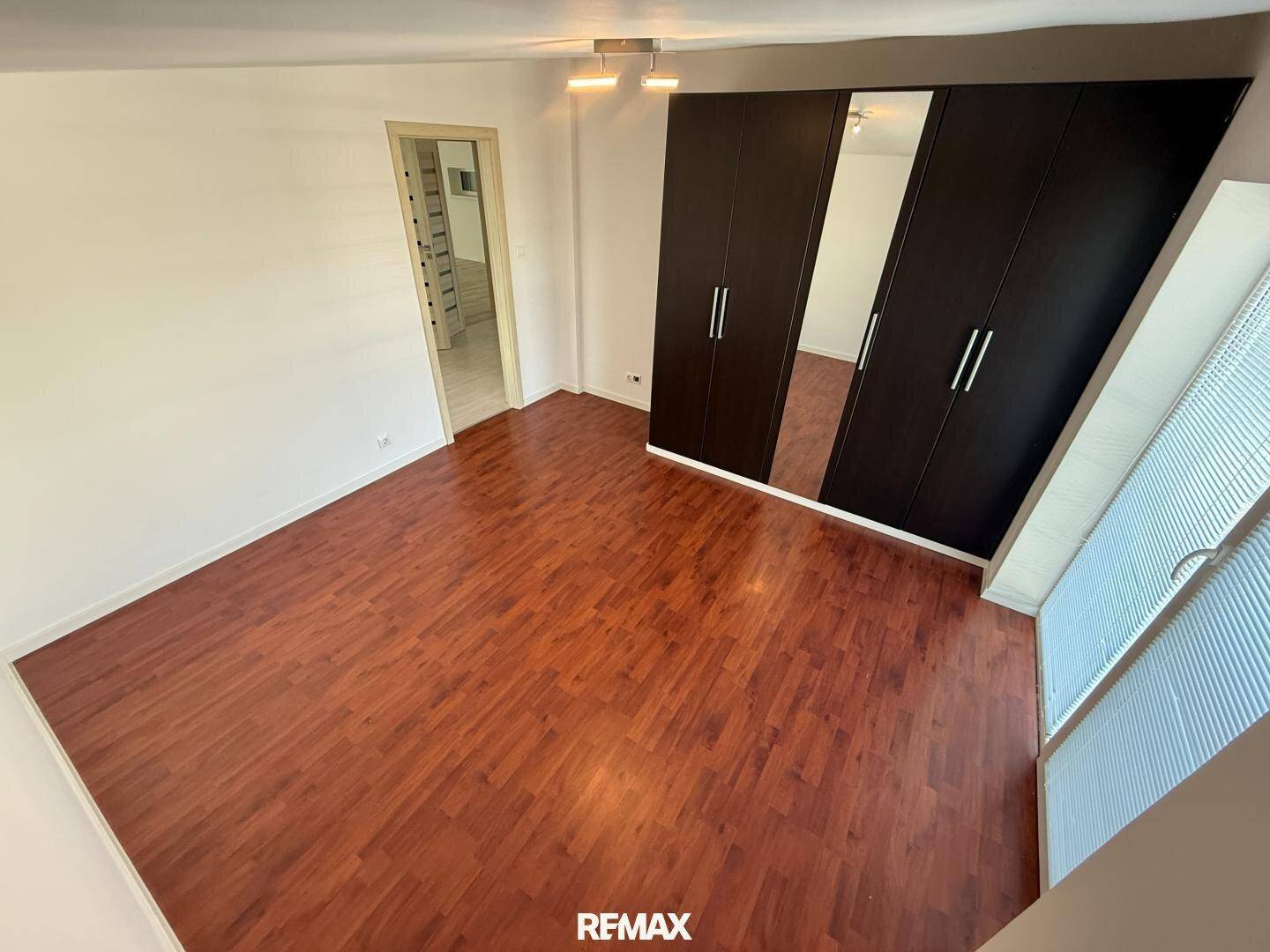 Geräumiges Schlafzimmer mit dunklem Laminatboden und großem Spiegelschrank.