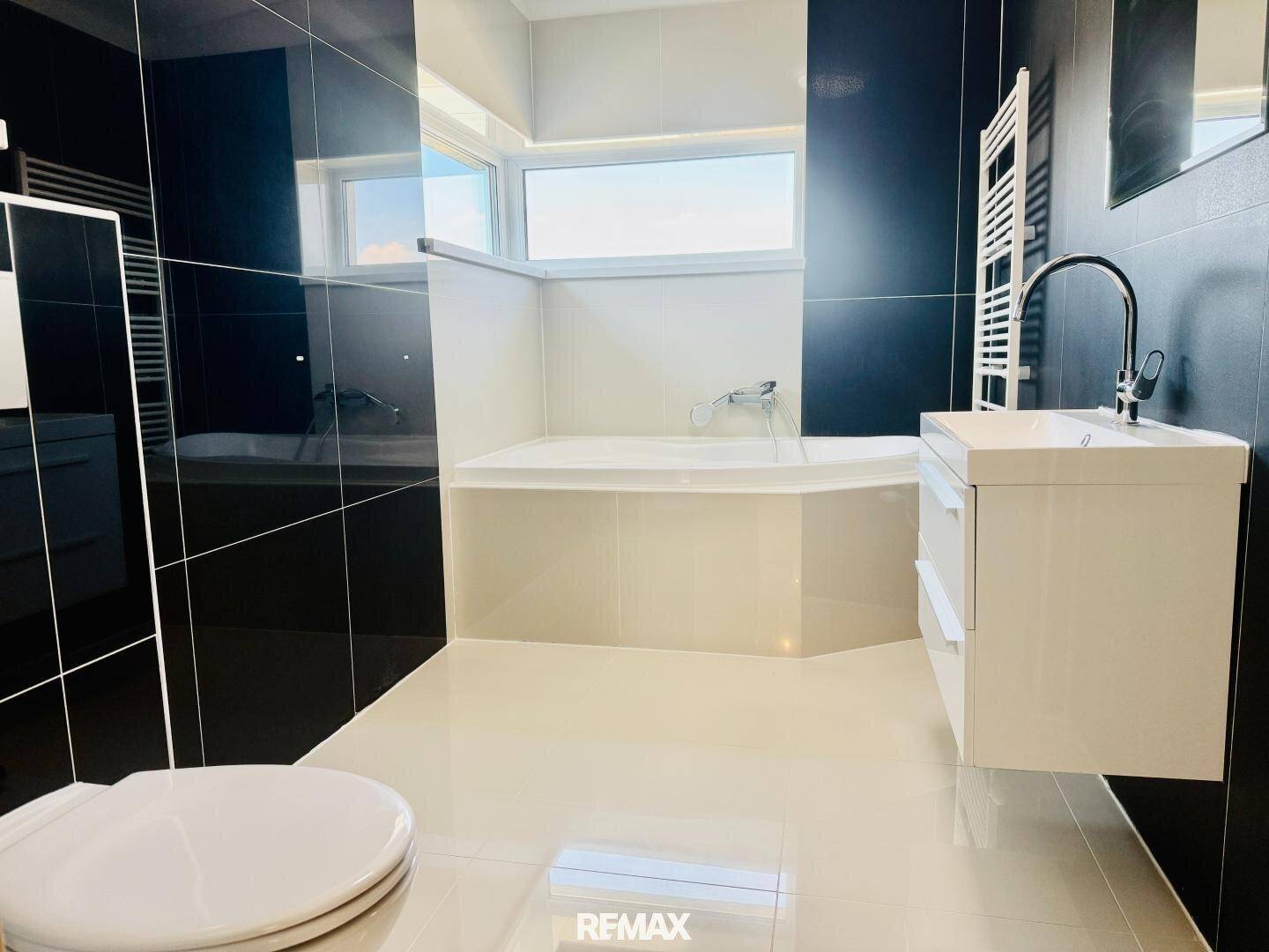 Stilvolles Badezimmer mit glänzenden schwarzen Fliesen, Eckbadewanne und modernem Waschbecken.