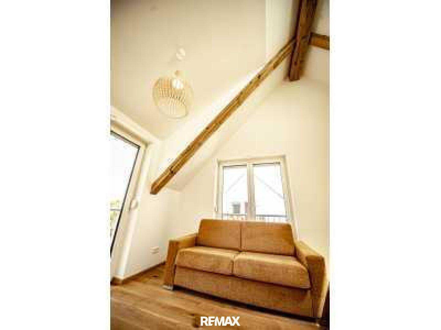 Gemütlicher Wohnbereich im Dachgeschoss mit Sofa, Holzbalken und viel natürlichem Licht.