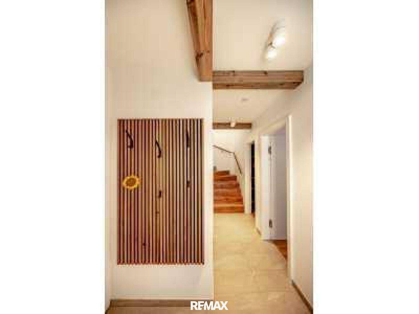 Heller Flur mit Holzbalken, Garderobe und Treppenaufgang.