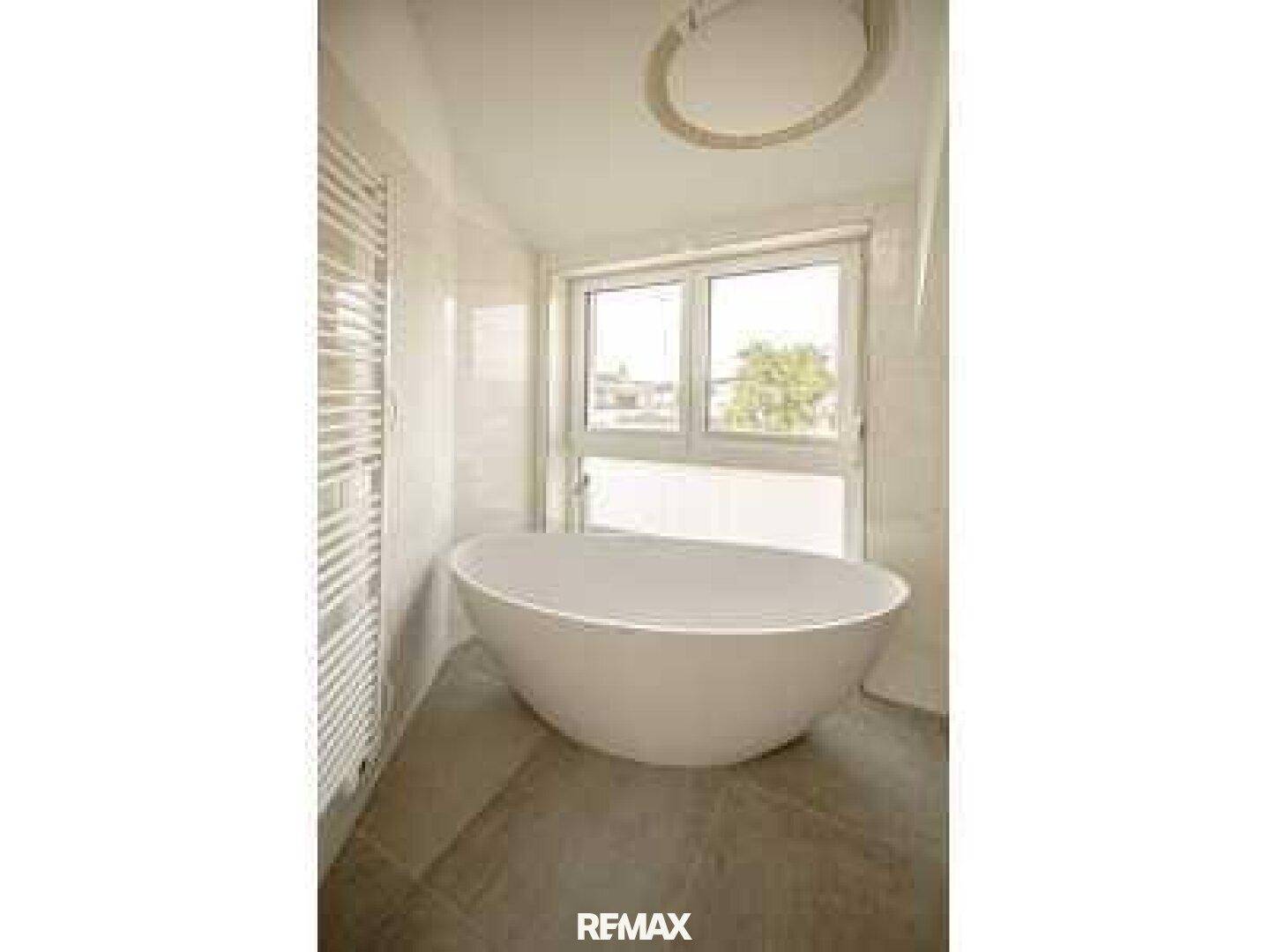 Modernes Badezimmer mit freistehender Badewanne und großem Fenster für viel Licht.