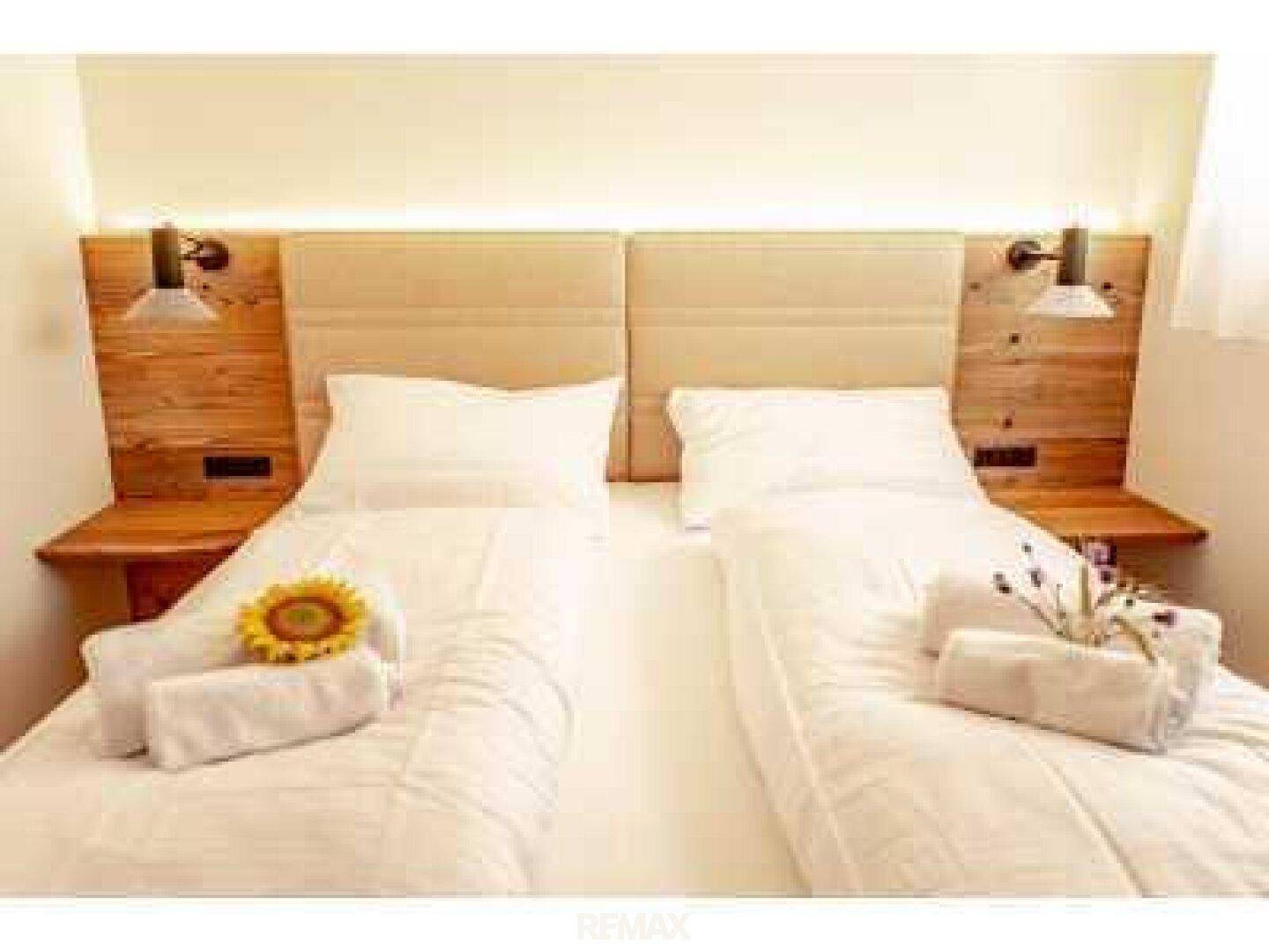Gemütliches Schlafzimmer mit zwei Einzelbetten, Holz-Kopfteil und Wandleuchten.