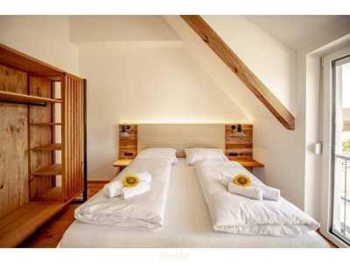 Helles Schlafzimmer im Dachgeschoss mit zwei Einzelbetten, Holzbalken und Schrägdach.