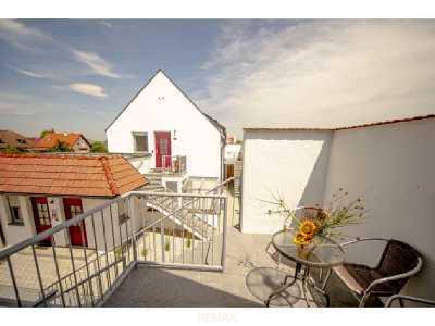 Sonniger Außenbereich mit Sitzgelegenheiten und Blick auf den Innenhof und umliegende Gebäude.
