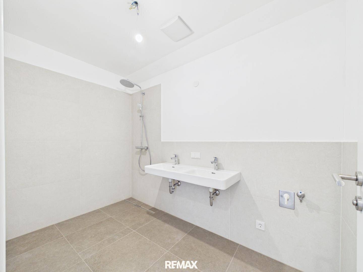 Modernes Badezimmer mit Doppelwaschbecken, Dusche und hellen Fliesen.