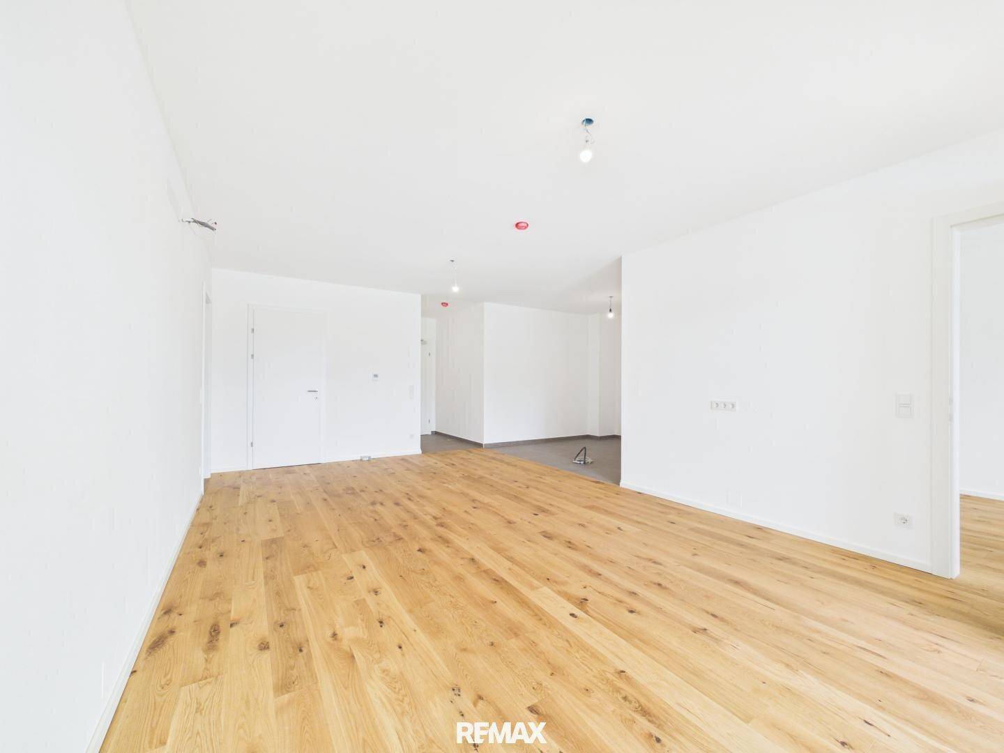 Leerer Wohnbereich mit hellem Holzboden und weißen Wänden, ideal für individuelle Einrichtung.