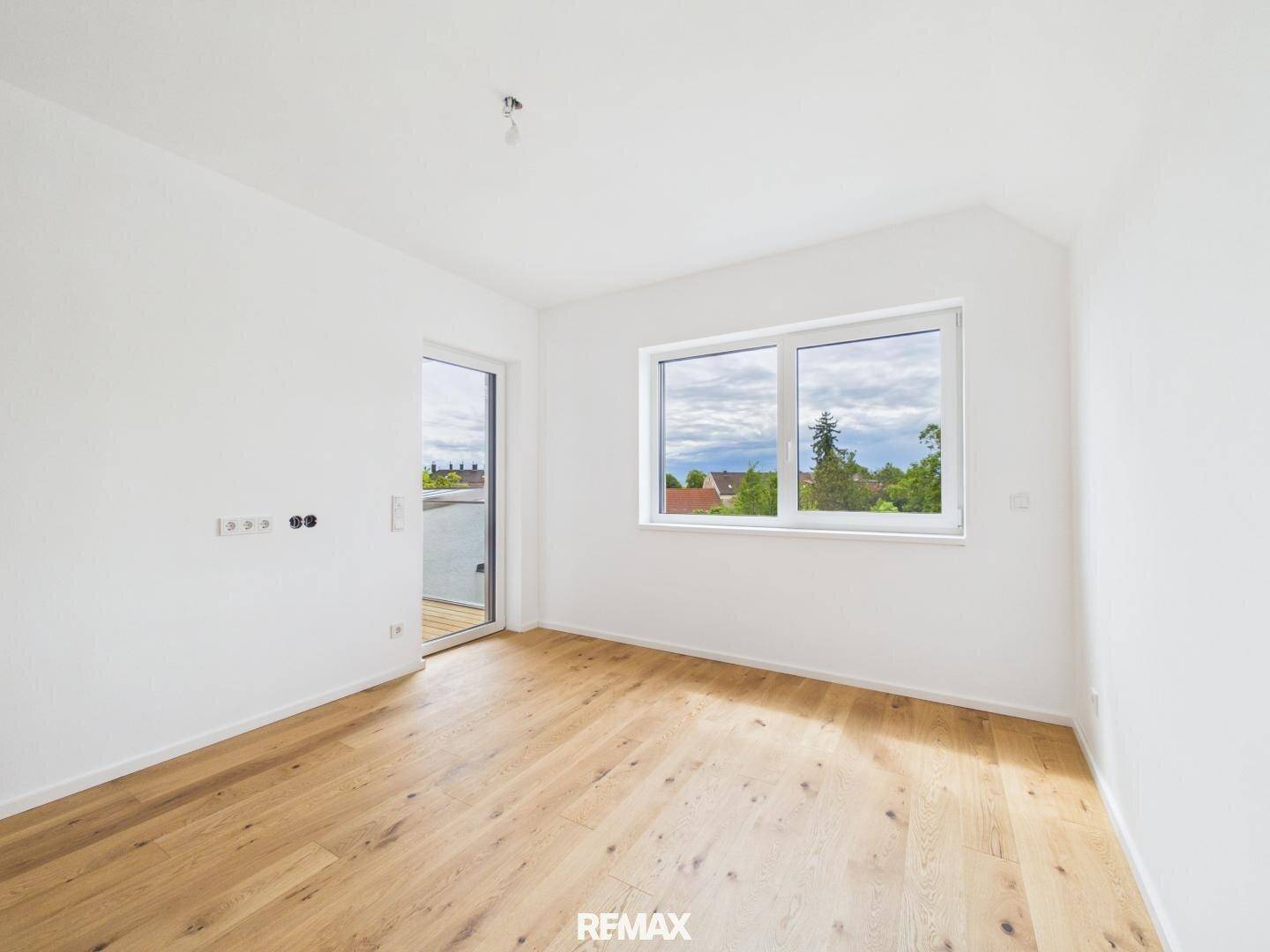 Helles Zimmer mit Holzboden und großem Fenster, bietet Zugang zu einem Außenbereich.