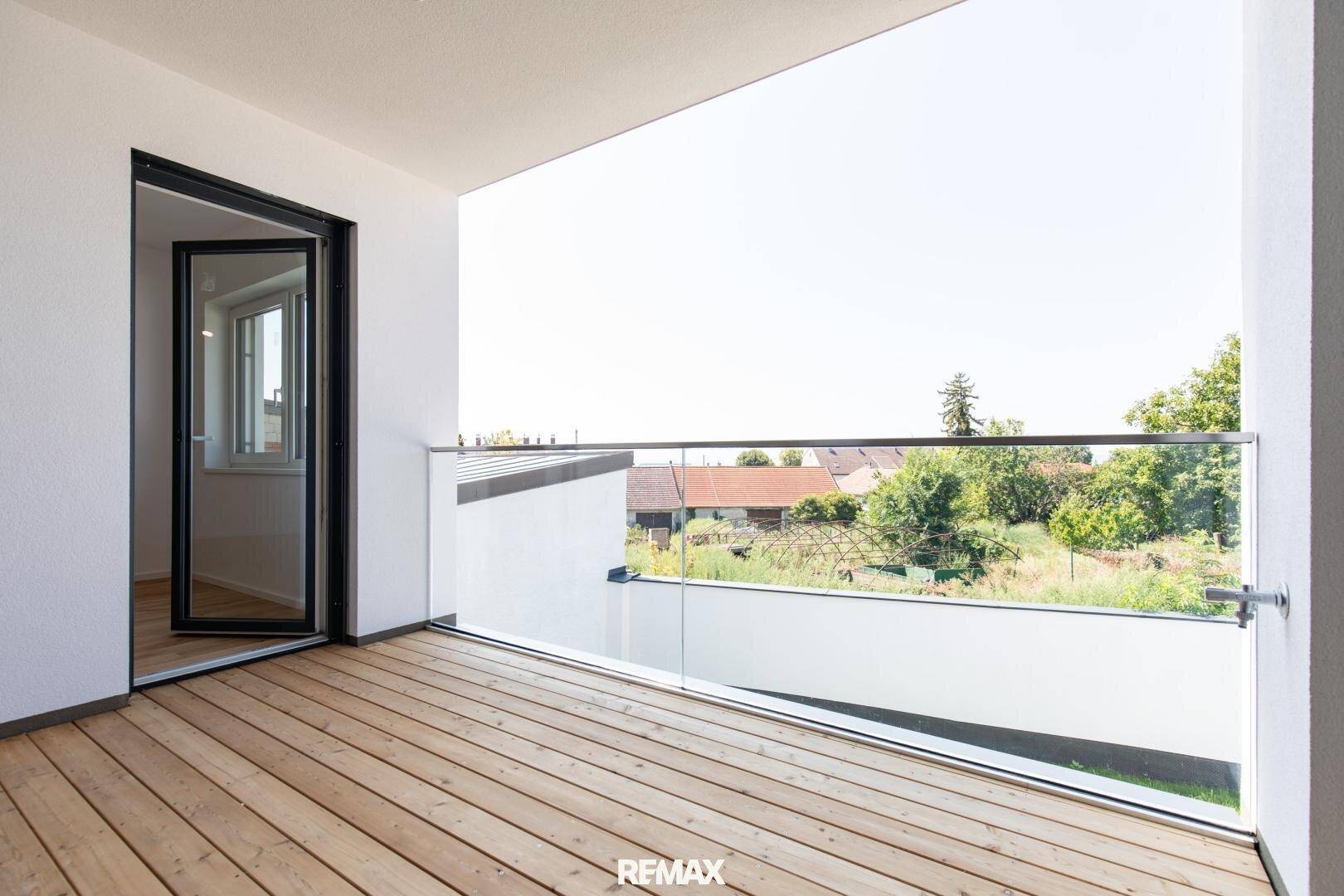 Heller Balkon mit Holzboden und Glasgeländer, bietet eine weite Aussicht.