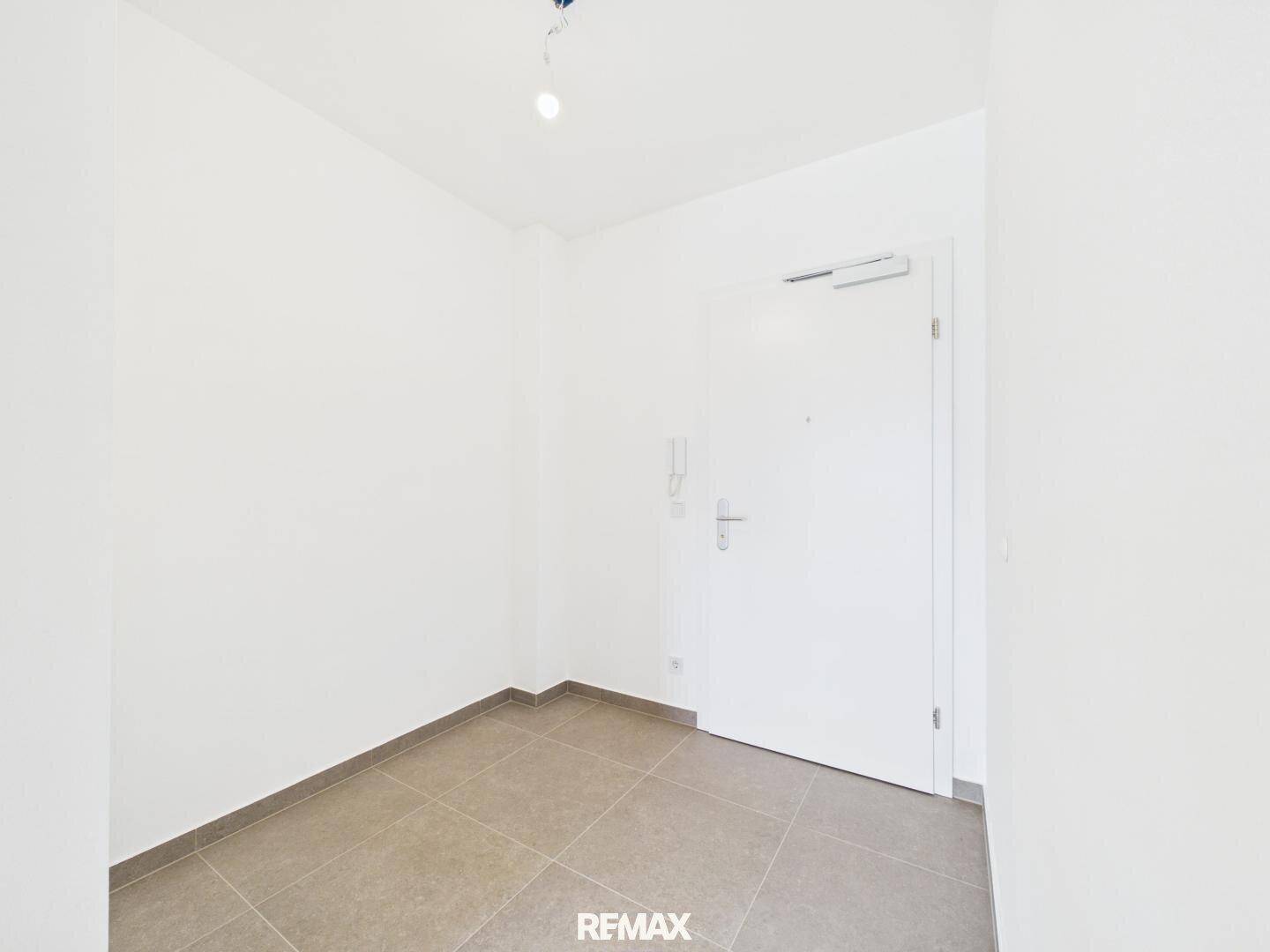 Heller Eingangsbereich mit Fliesenboden und weißer Eingangstür in einem Neubau.
