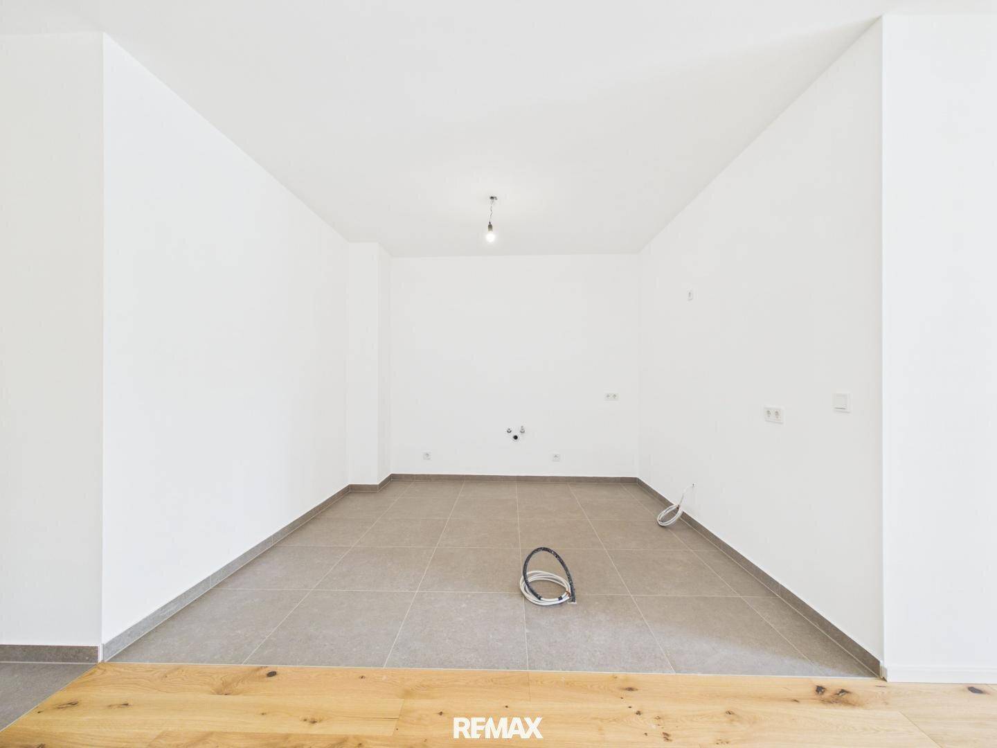 Unmöblierter Küchenbereich mit Fliesenboden und Anschlüssen, bereit für die Installation.