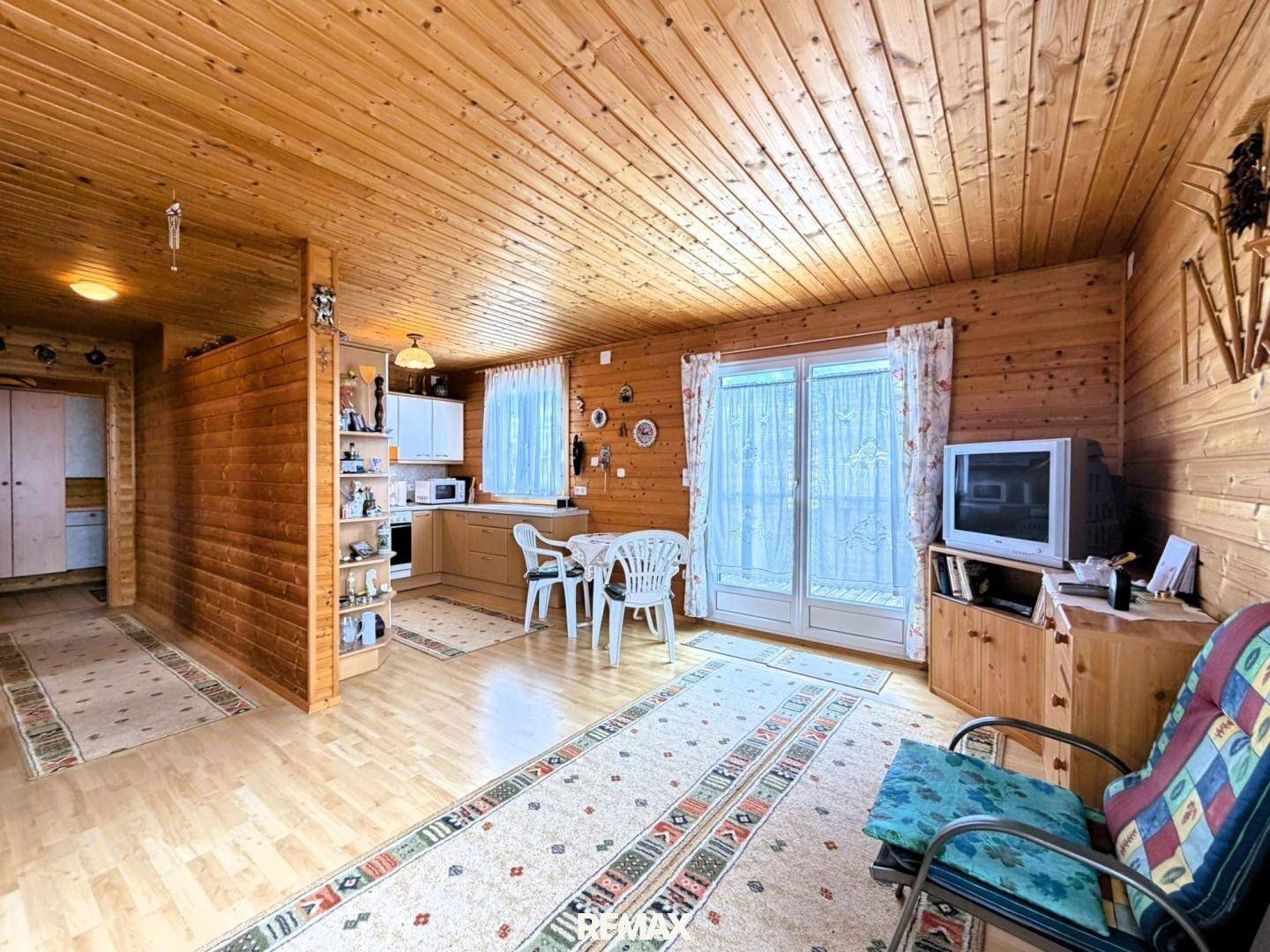 Heller Wohnbereich mit Holzwänden und -decke, Essbereich und Zugang zur Terrasse durch eine Glastür.