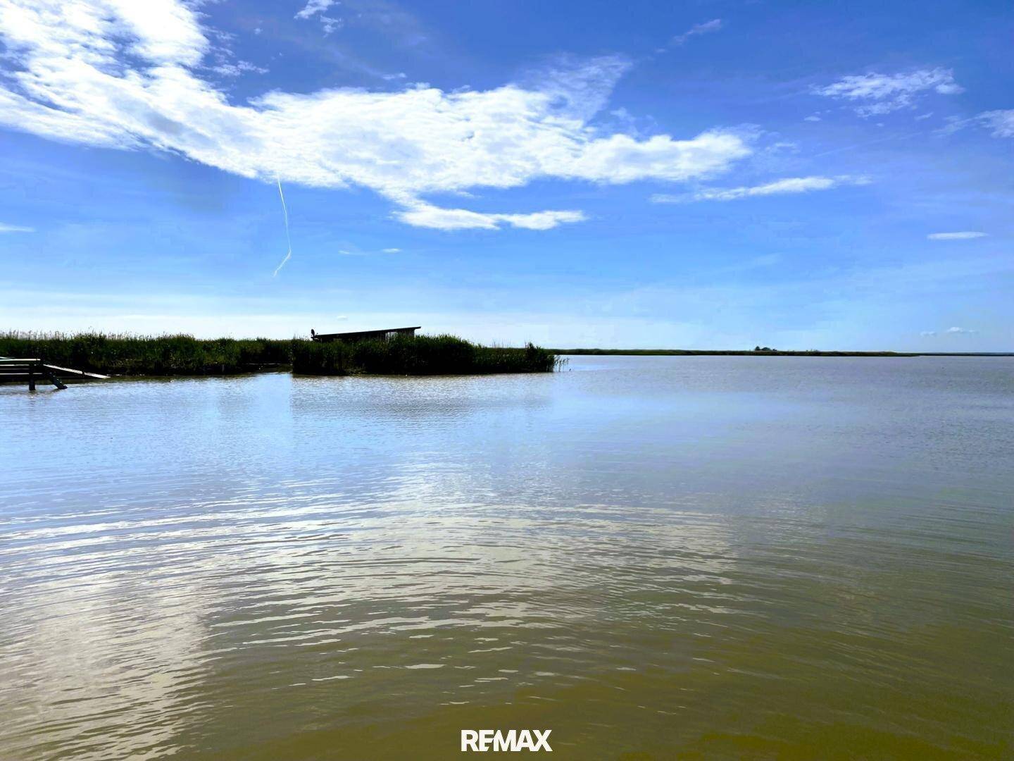 Weitläufige Wasserlandschaft unter blauem Himmel mit einigen Schilfinseln in der Ferne.