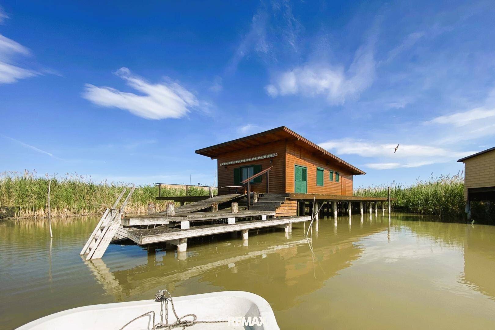 Charmantes Holzhaus auf Stelzen über dem Wasser, umgeben von Schilf, mit einer breiten Holzterrasse.