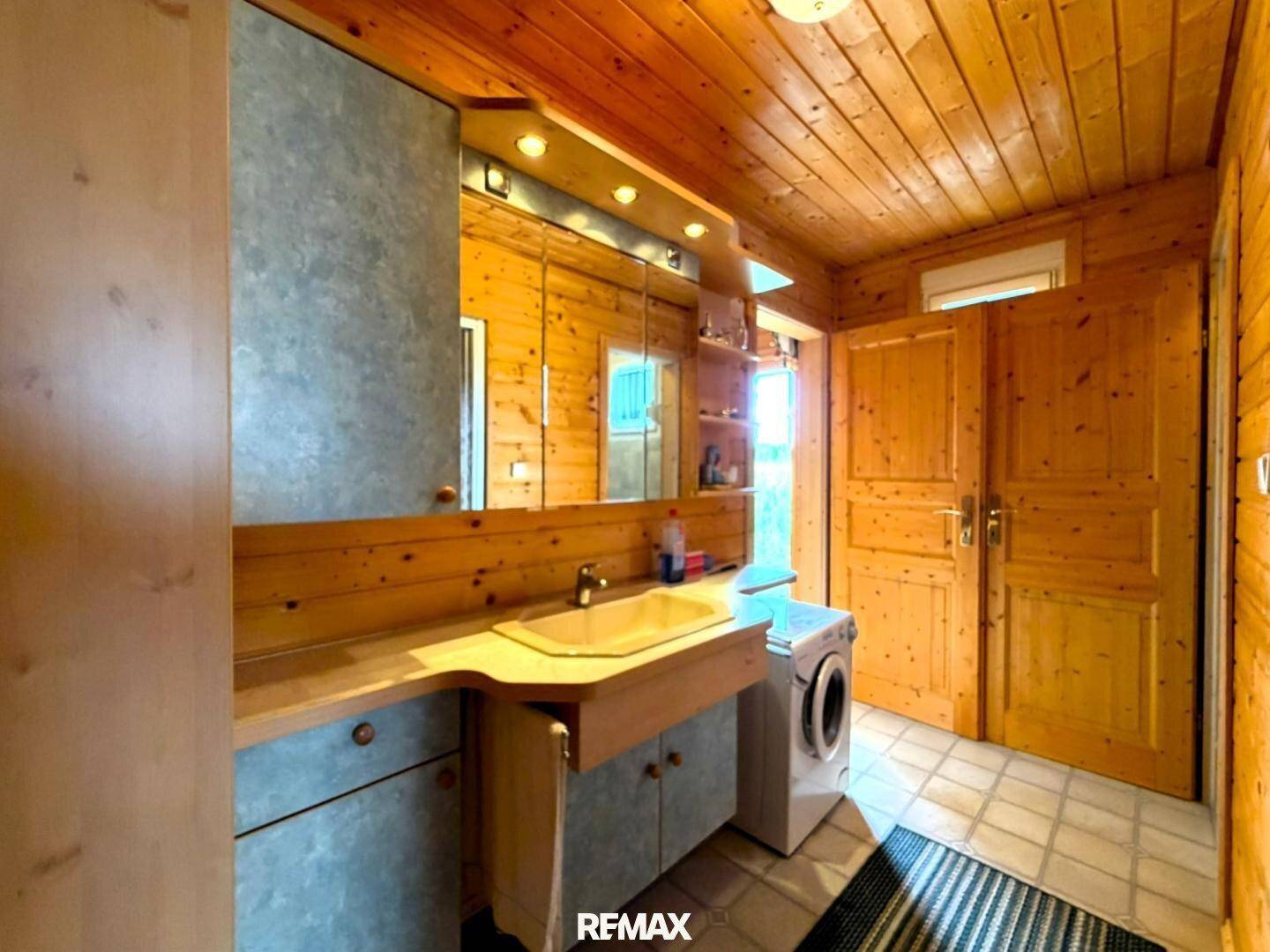Badezimmer mit Holzvertäfelung, Waschbecken, Spiegelschrank und integrierter Waschmaschine.