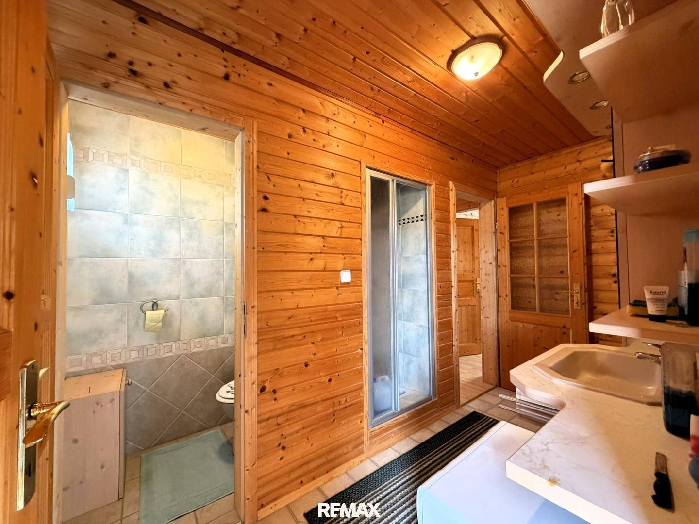 Badezimmer mit Duschkabine und separatem WC, komplett in Holz und Fliesen gehalten.